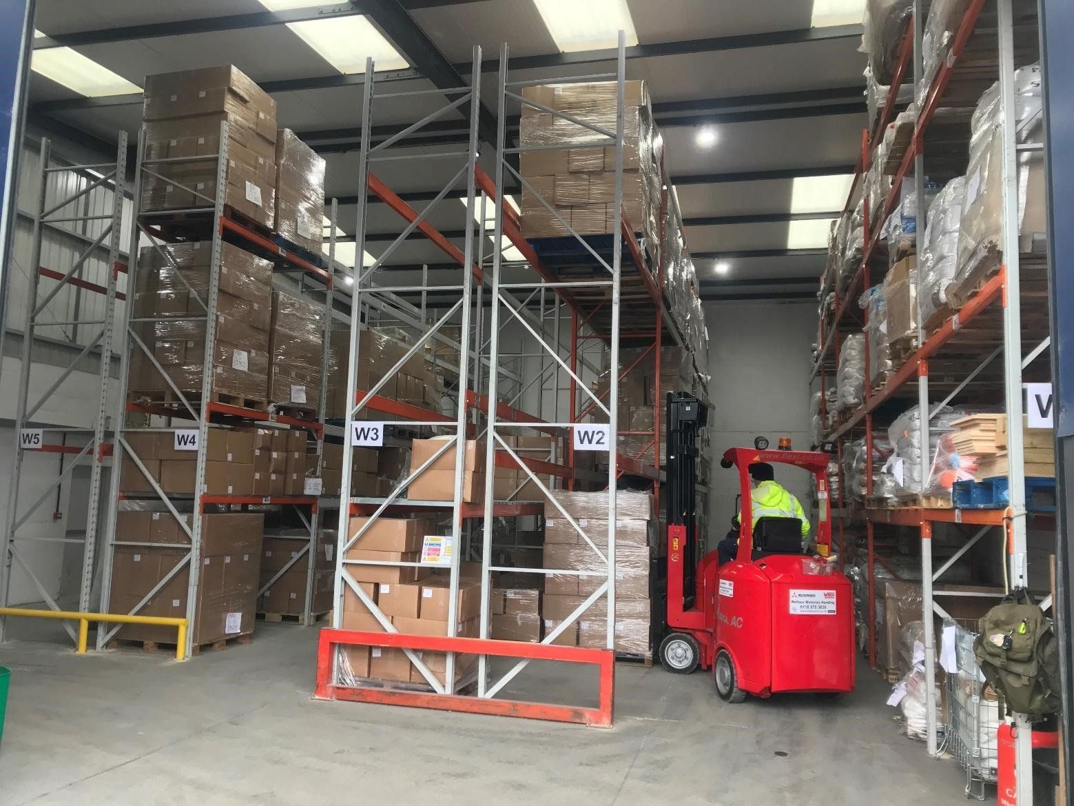 A man is driving a red forklift in a large warehouse.