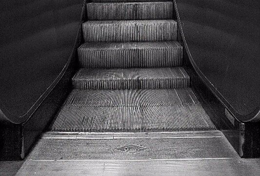 A black and white photo of an escalator going up.