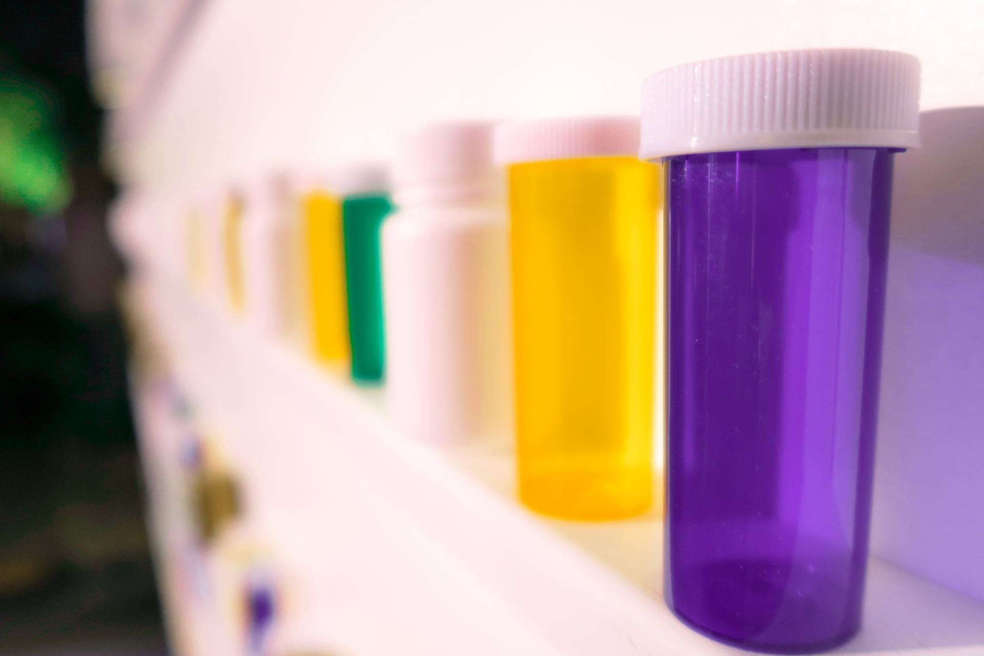 A row of bottles of different colors are lined up on a shelf.
