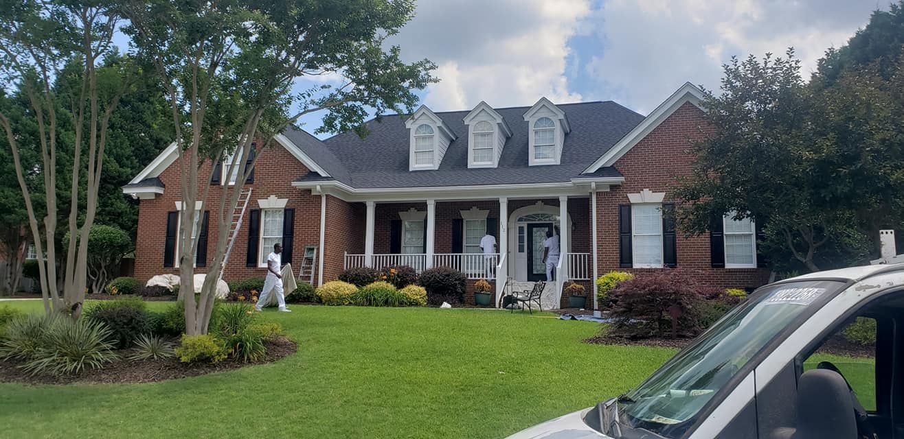 House with red brick exterior, white trim, black shutters, and three dormers being painted by workers.