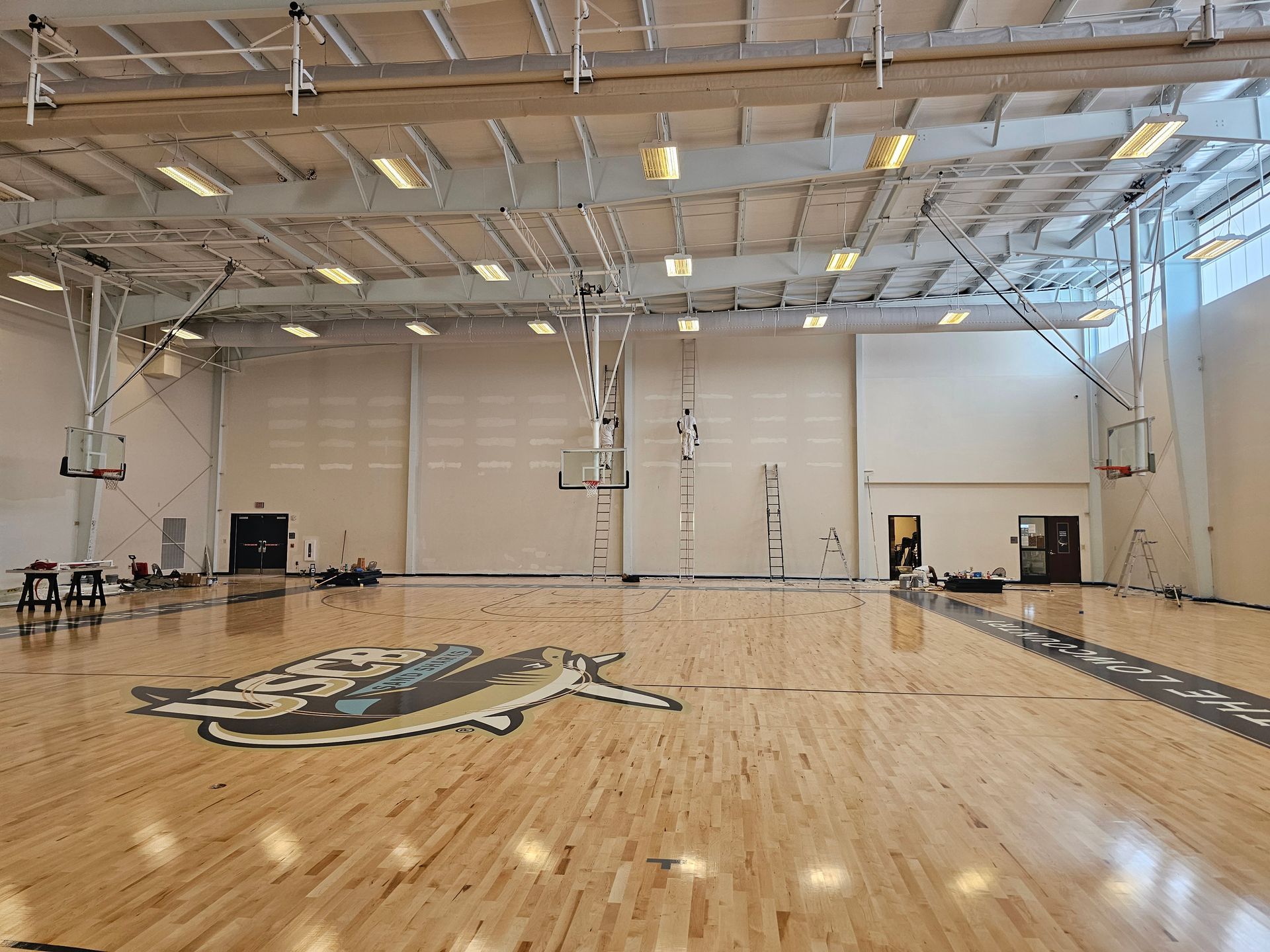 Empty basketball court with wooden floor, hoops, and ceiling lights.
