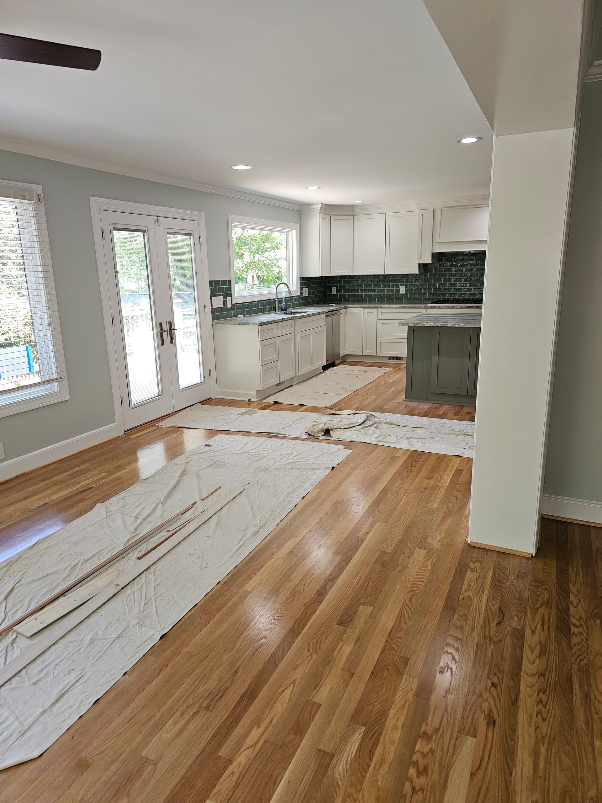 Hardwood floors in a renovated kitchen, white cabinets, green backsplash, French doors, and light green walls.