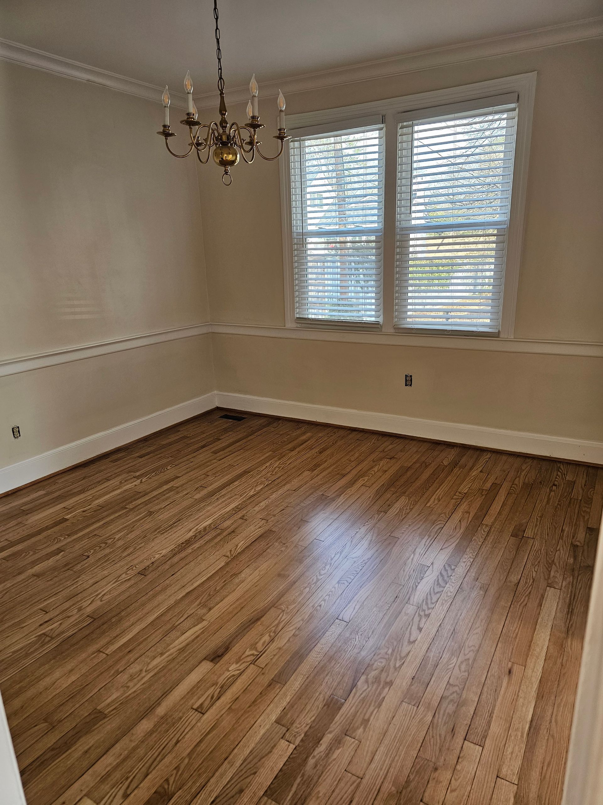 Empty dining room with hardwood floors, chandelier, and window with blinds.