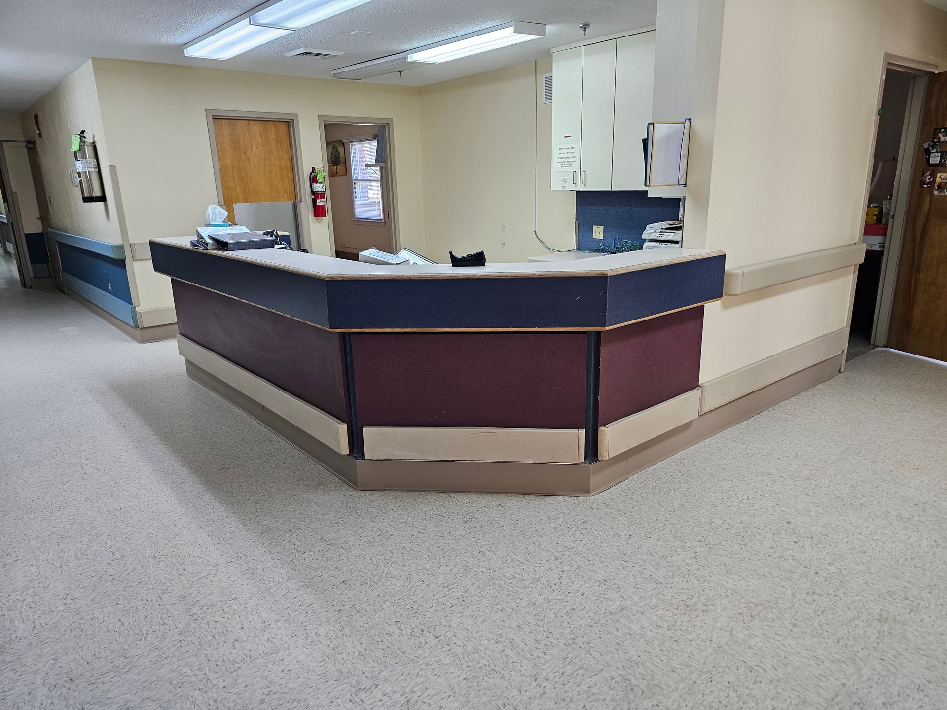 Reception desk in a medical facility hallway, with two doors, cabinets, and a beige and blue color scheme.