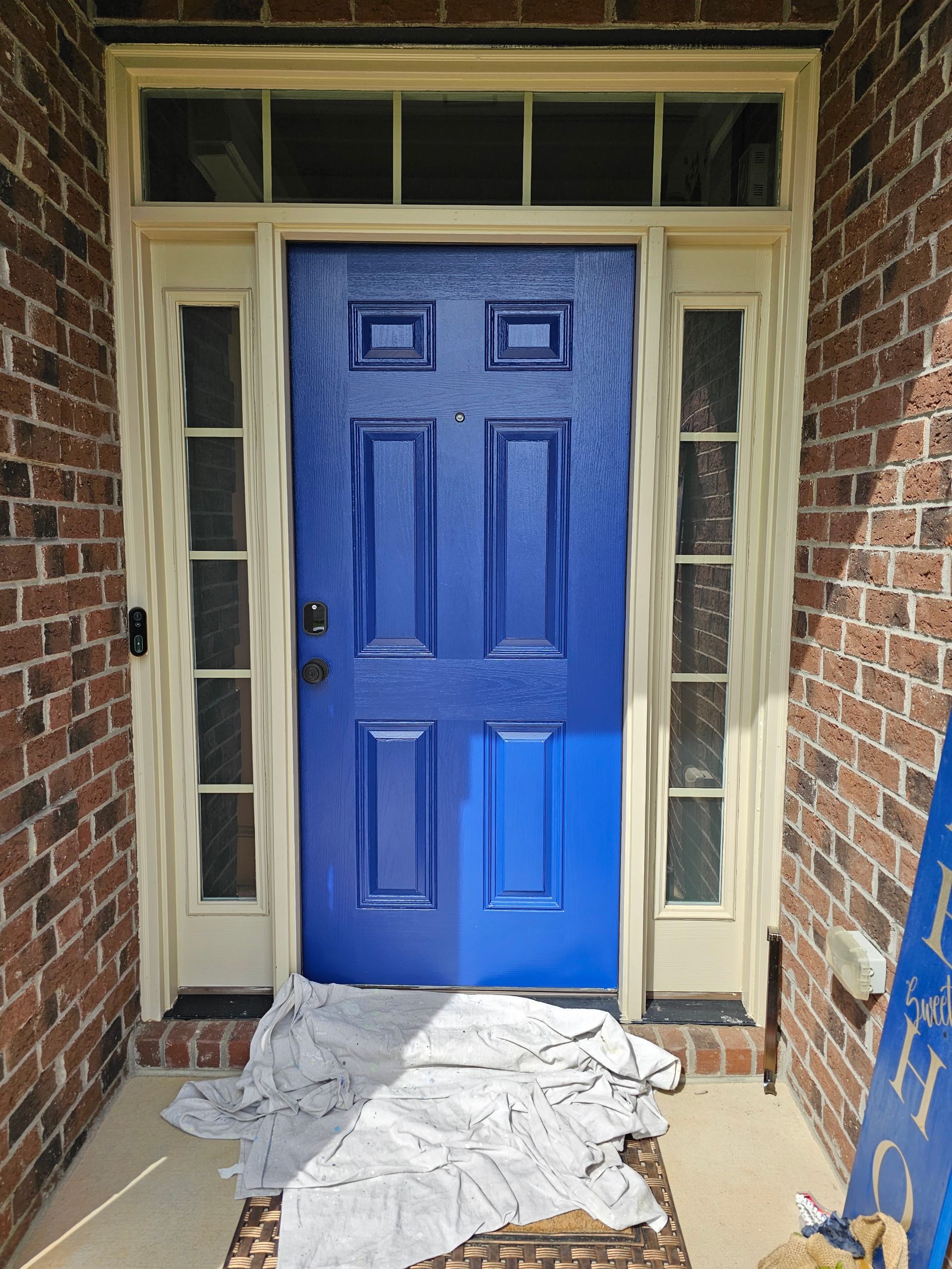 Blue painted front door with cream trim, brick exterior. Paint is being applied.