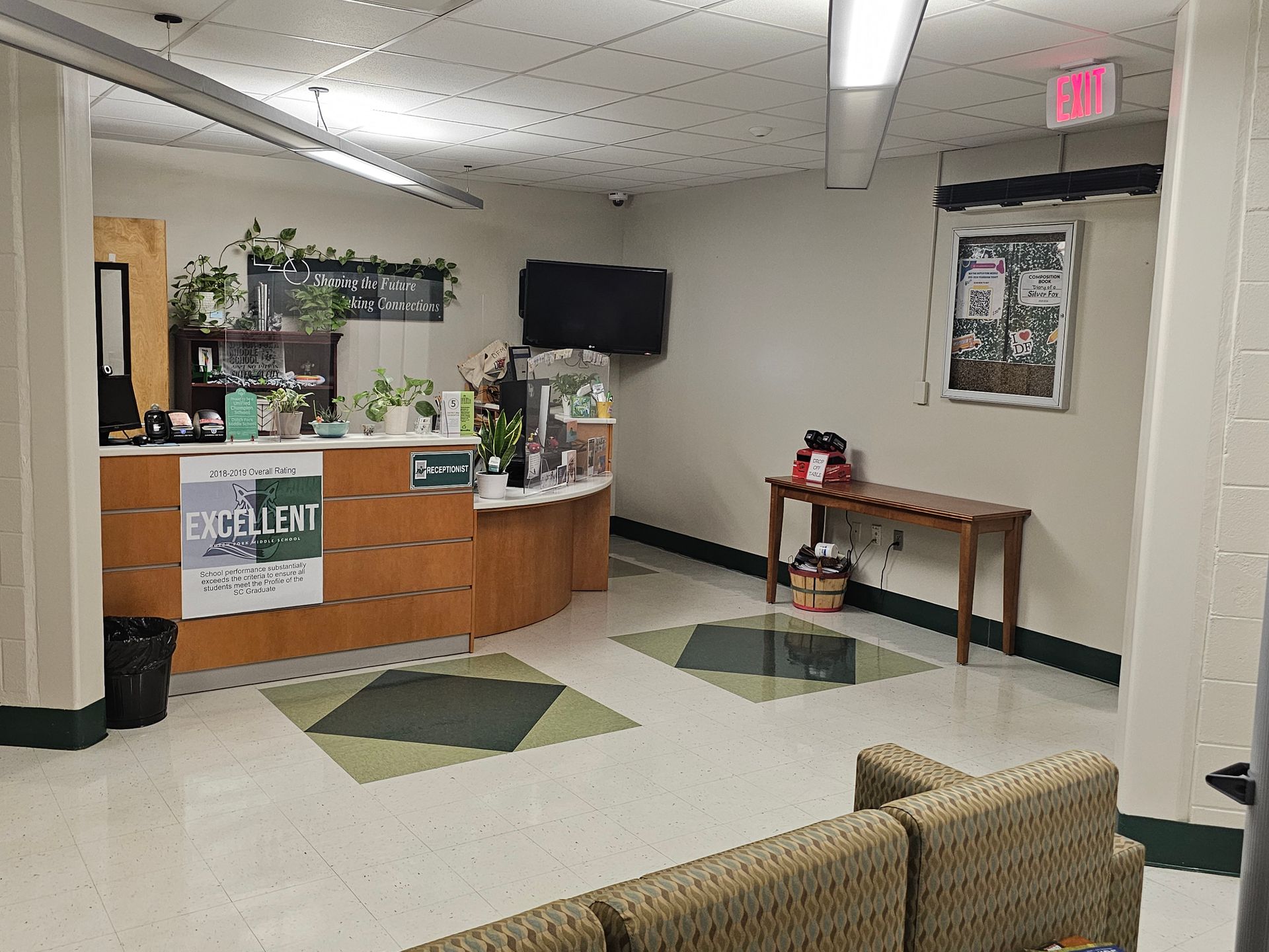 Reception area with curved desk, plants, TV, and waiting area with a couch.