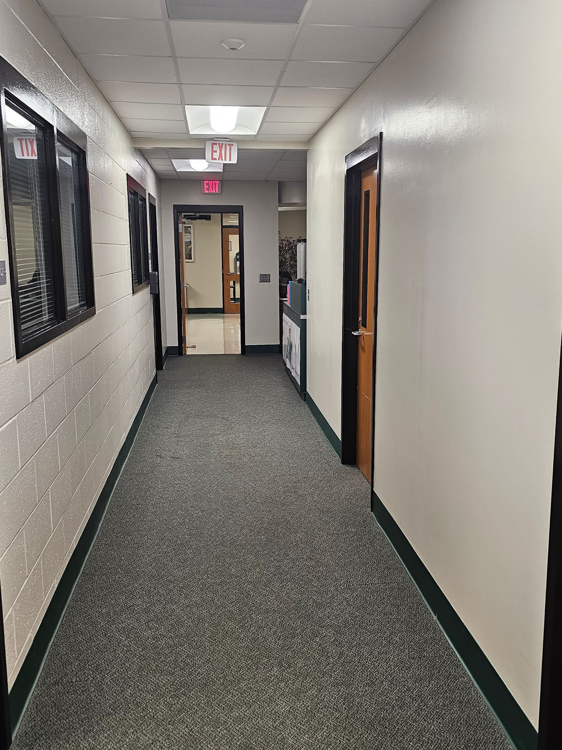 Hallway with windows on the left and doors on the right, leading to a door with an 