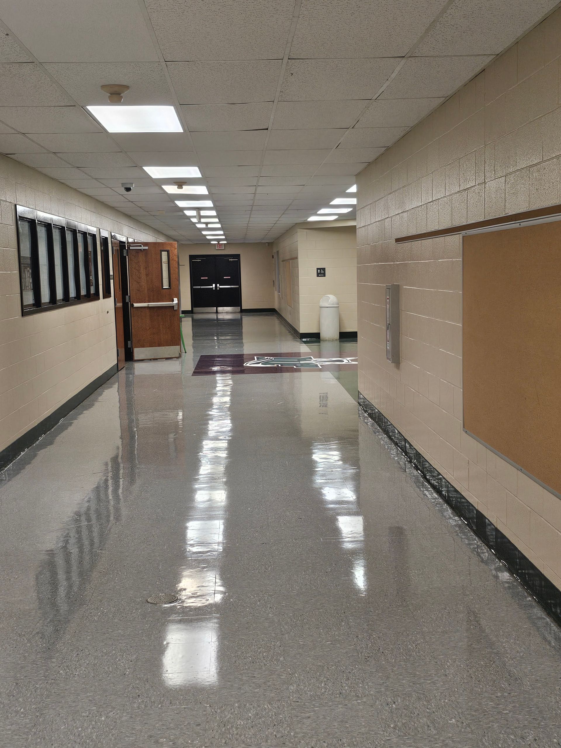 Empty school hallway with glossy floor, white walls, and closed doors.
