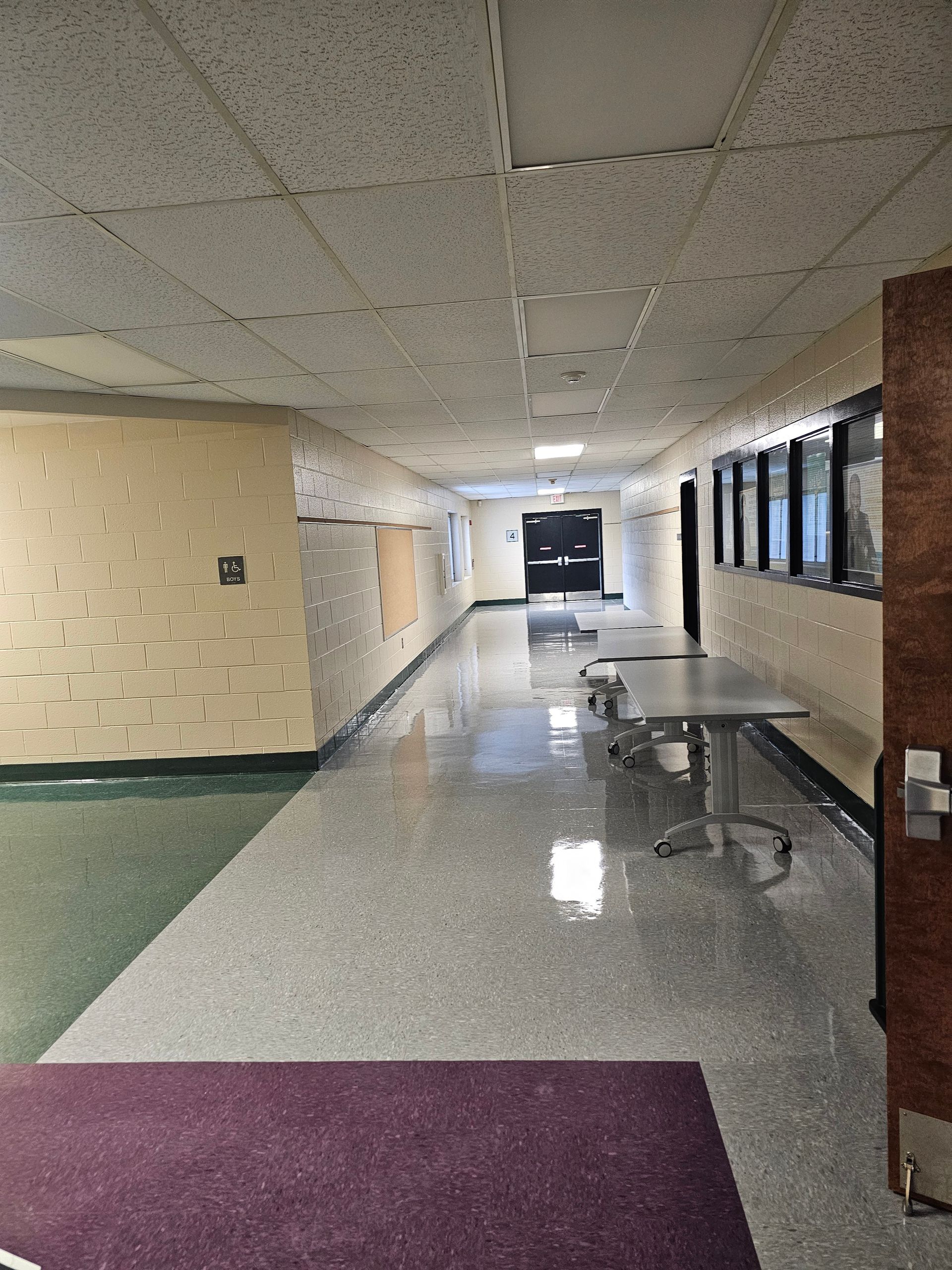 Hallway with speckled floor, tables, and a purple rug. Ceiling and walls. Sunlight coming in from right side windows.
