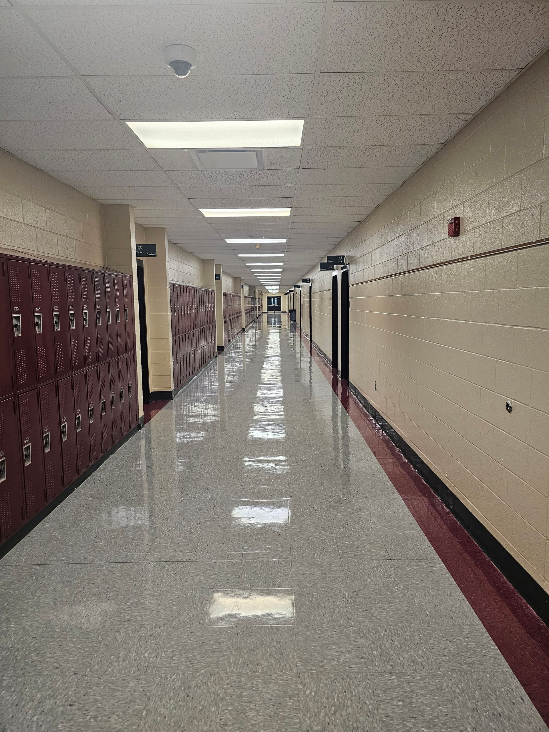 School hallway with lockers on the left, doors on the right, and bright ceiling lights.