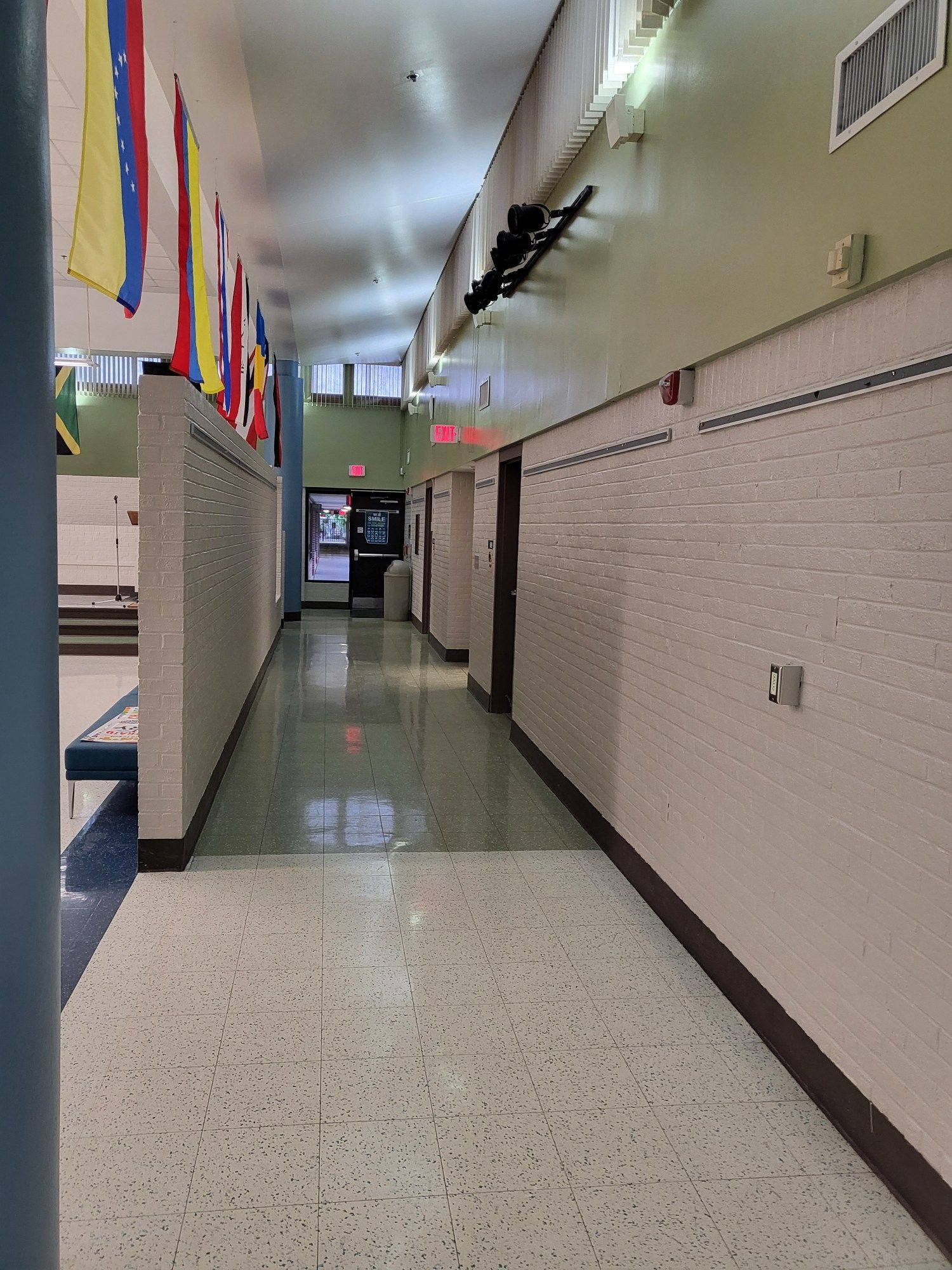 Hallway with flags, white brick walls, and doors. Green floor and ceiling with bright lights.