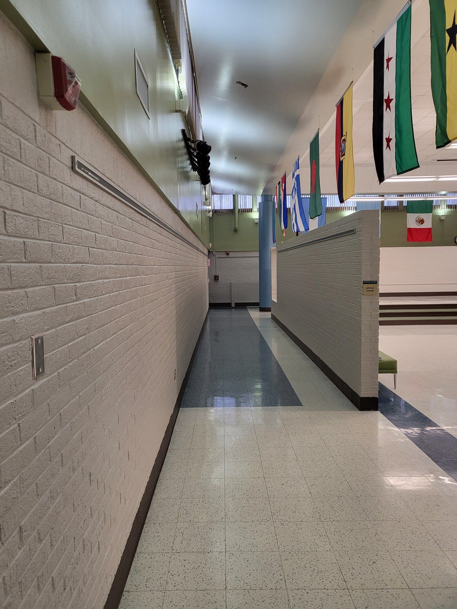 Hallway with brick wall and flags hanging from the ceiling. A blue and white tiled floor leads to a doorway.