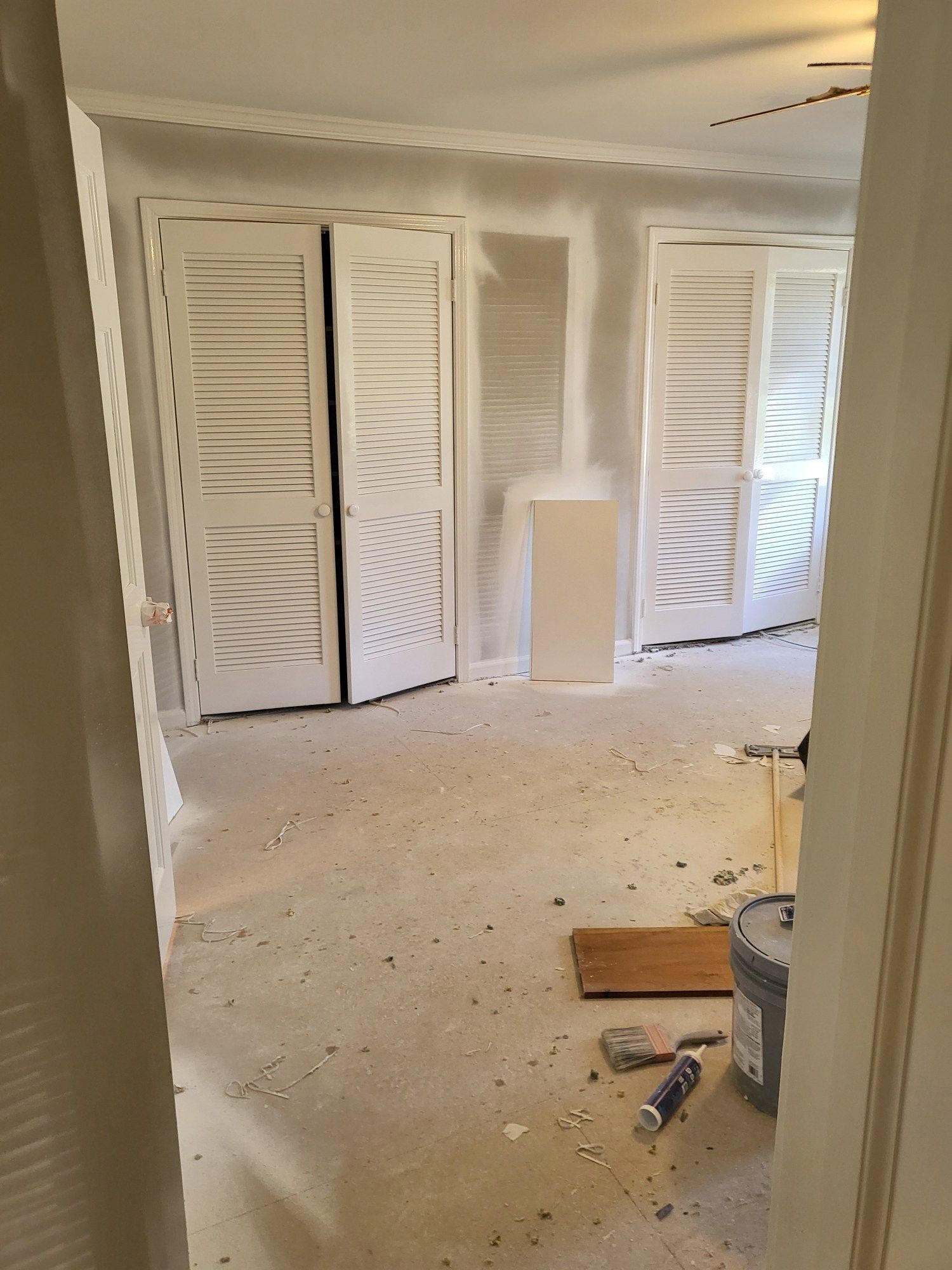 Interior room under construction, with white closet doors and drywall; tools on the floor.