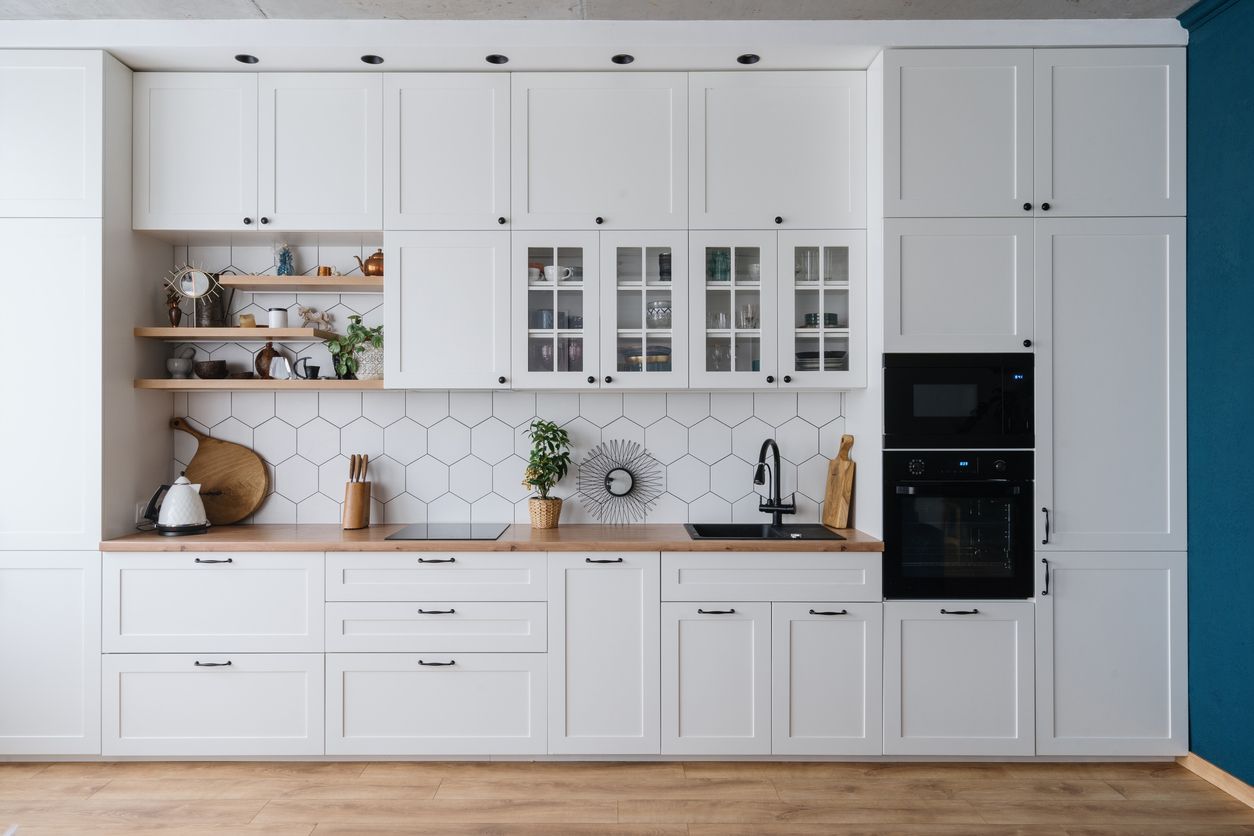 White kitchen with wooden countertops, hexagonal tile backsplash, and black appliances.