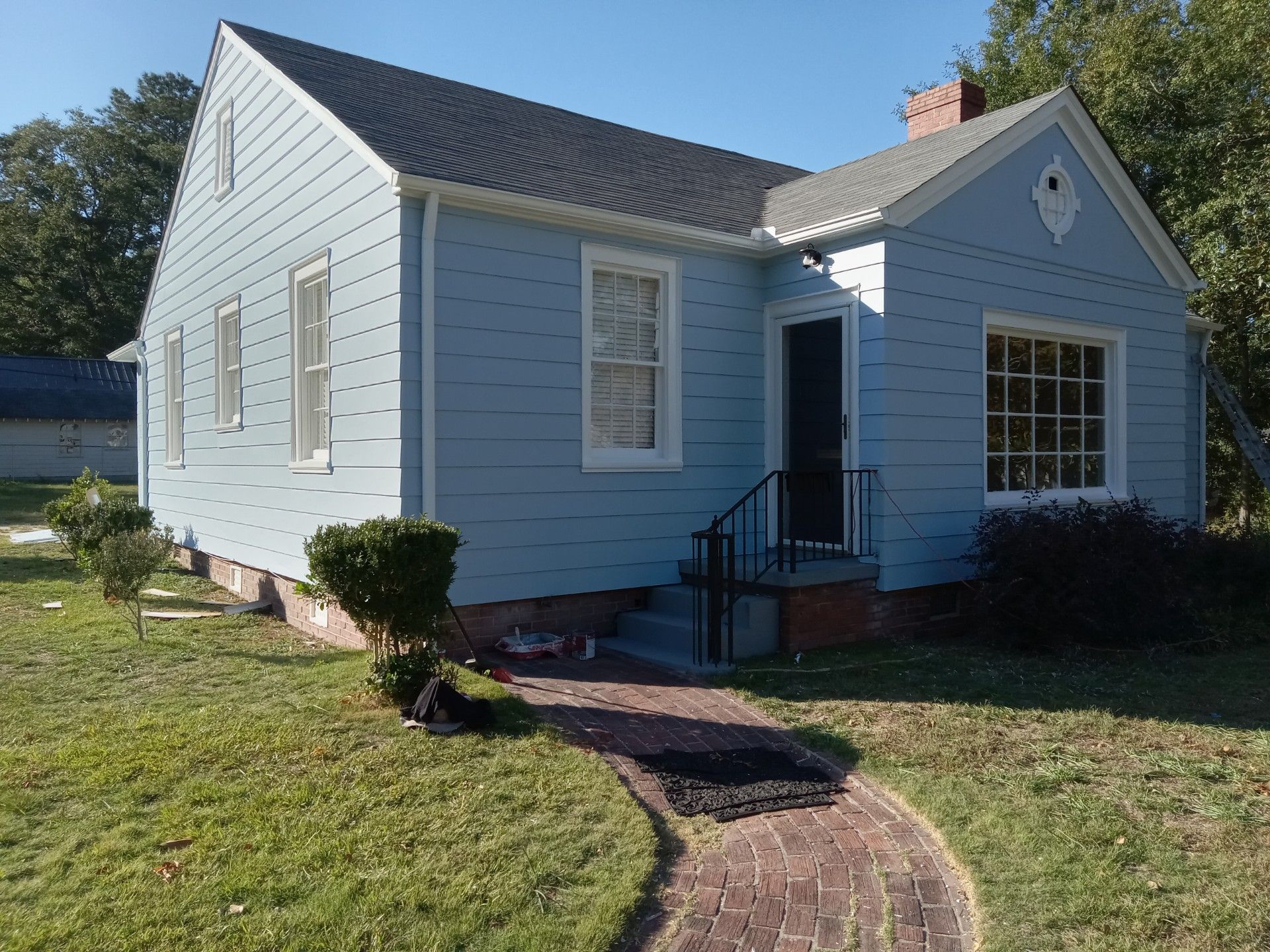 Blue house with brick walkway, black door, and green yard on a sunny day.
