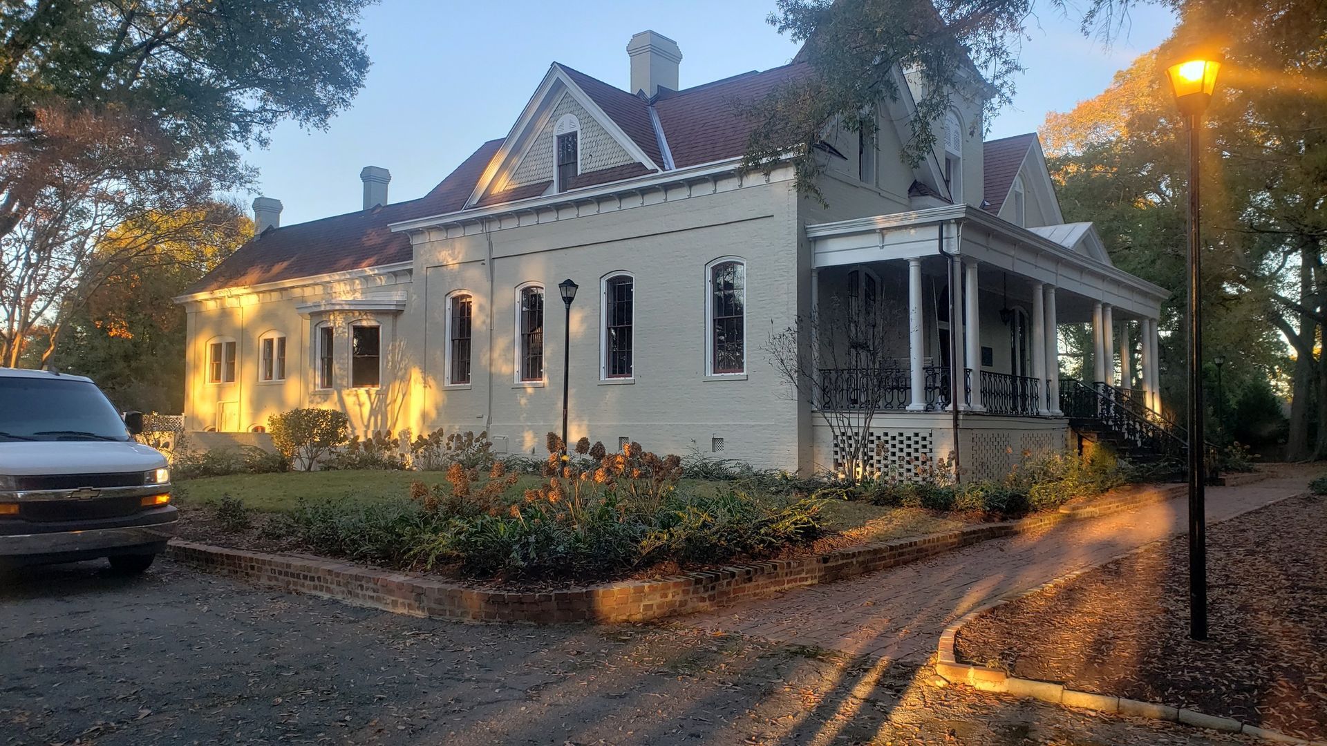 A large, light-colored house with a porch and red roof; a van is parked in the driveway at dusk.