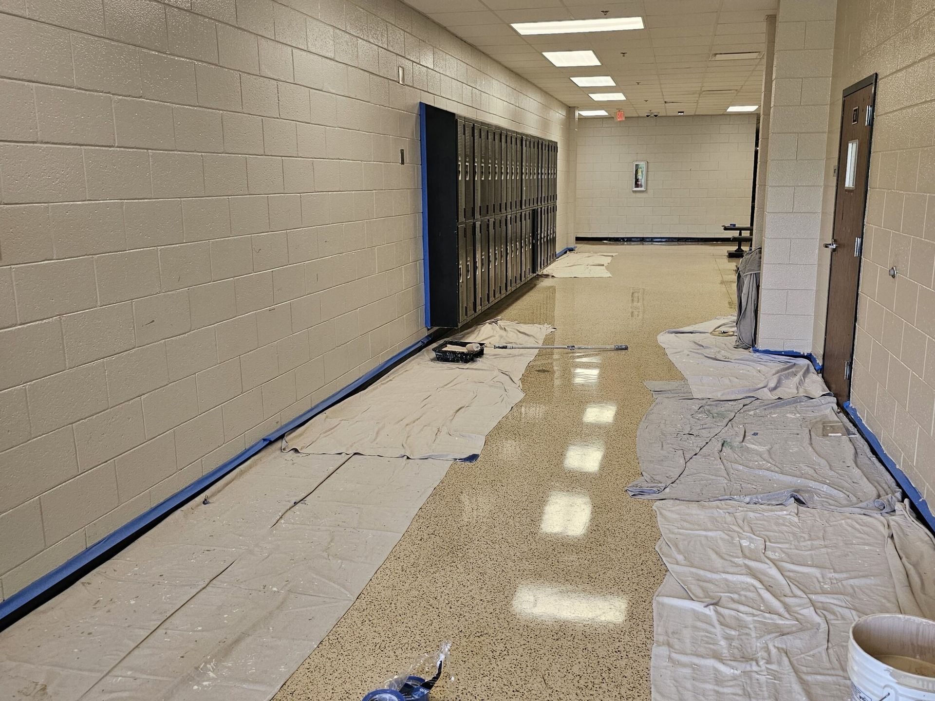 School hallway with paper covering floor, paint supplies, lockers, and door.
