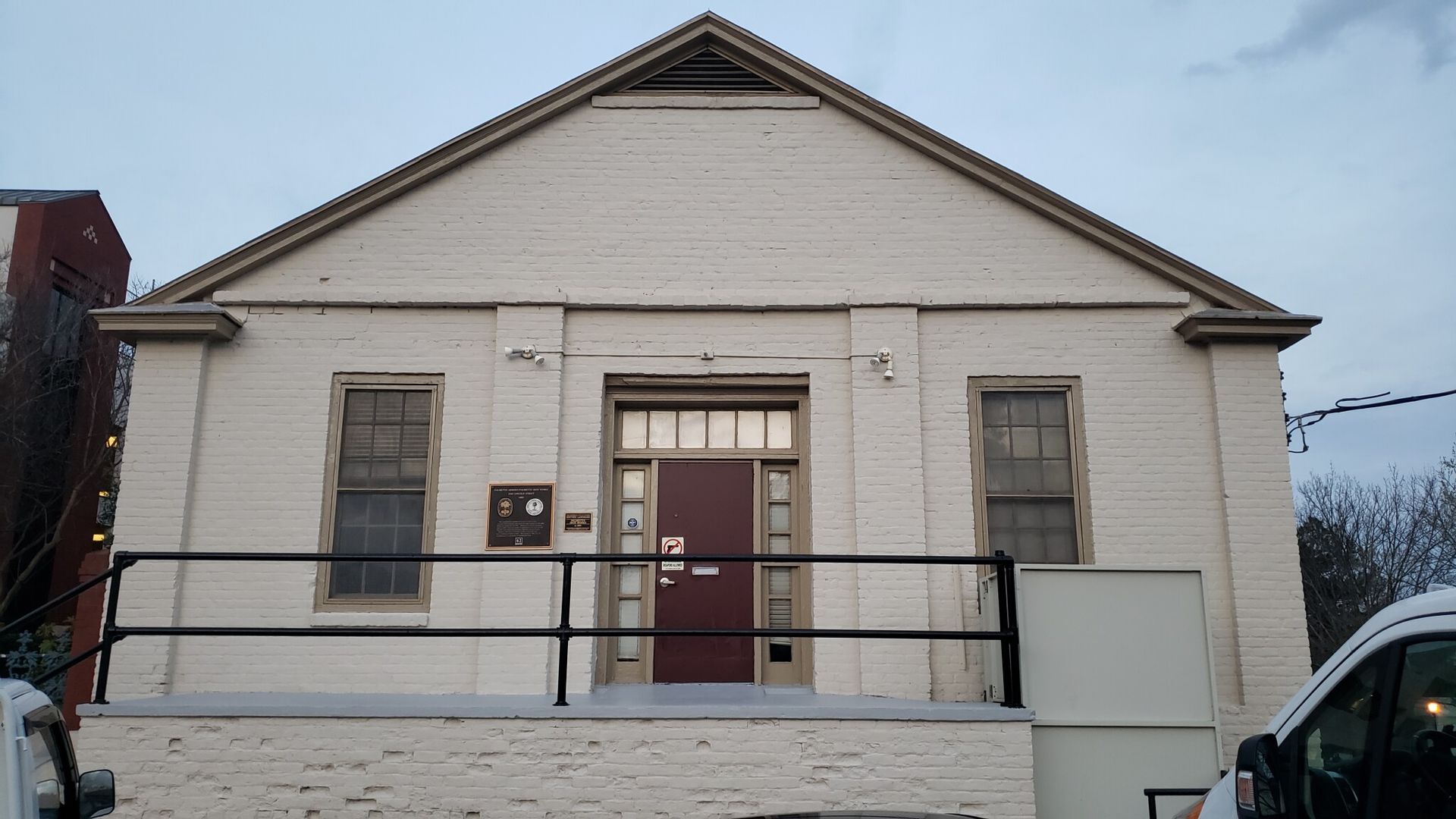 White brick building with gabled roof; brown door and windows. Snow on railing and roof.