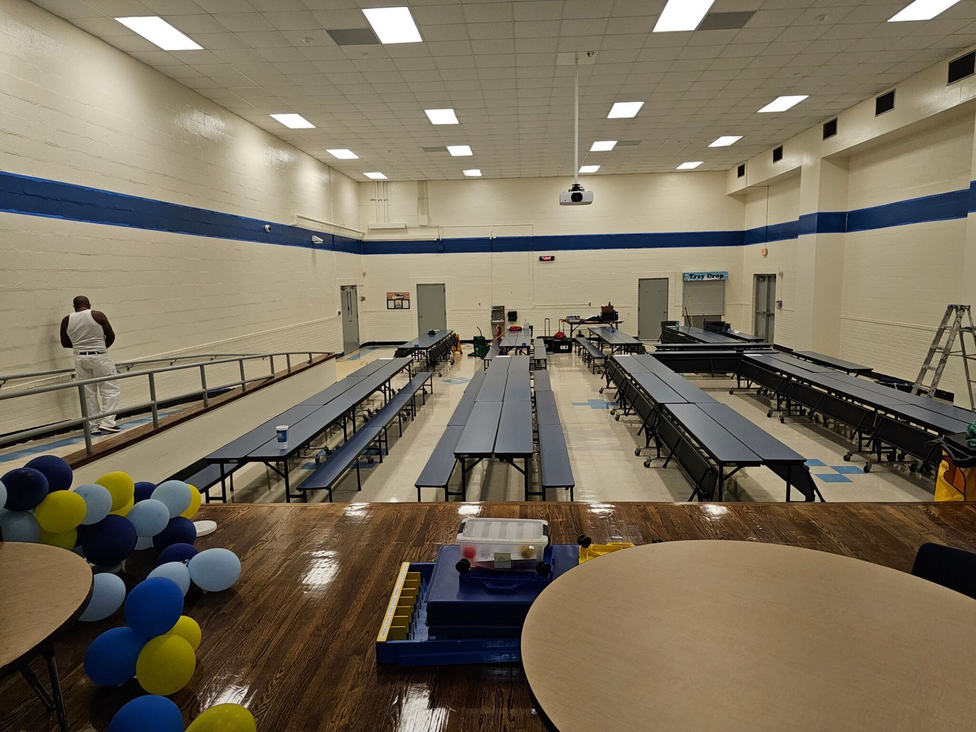 School cafeteria with blue tables, balloons, and a person painting.