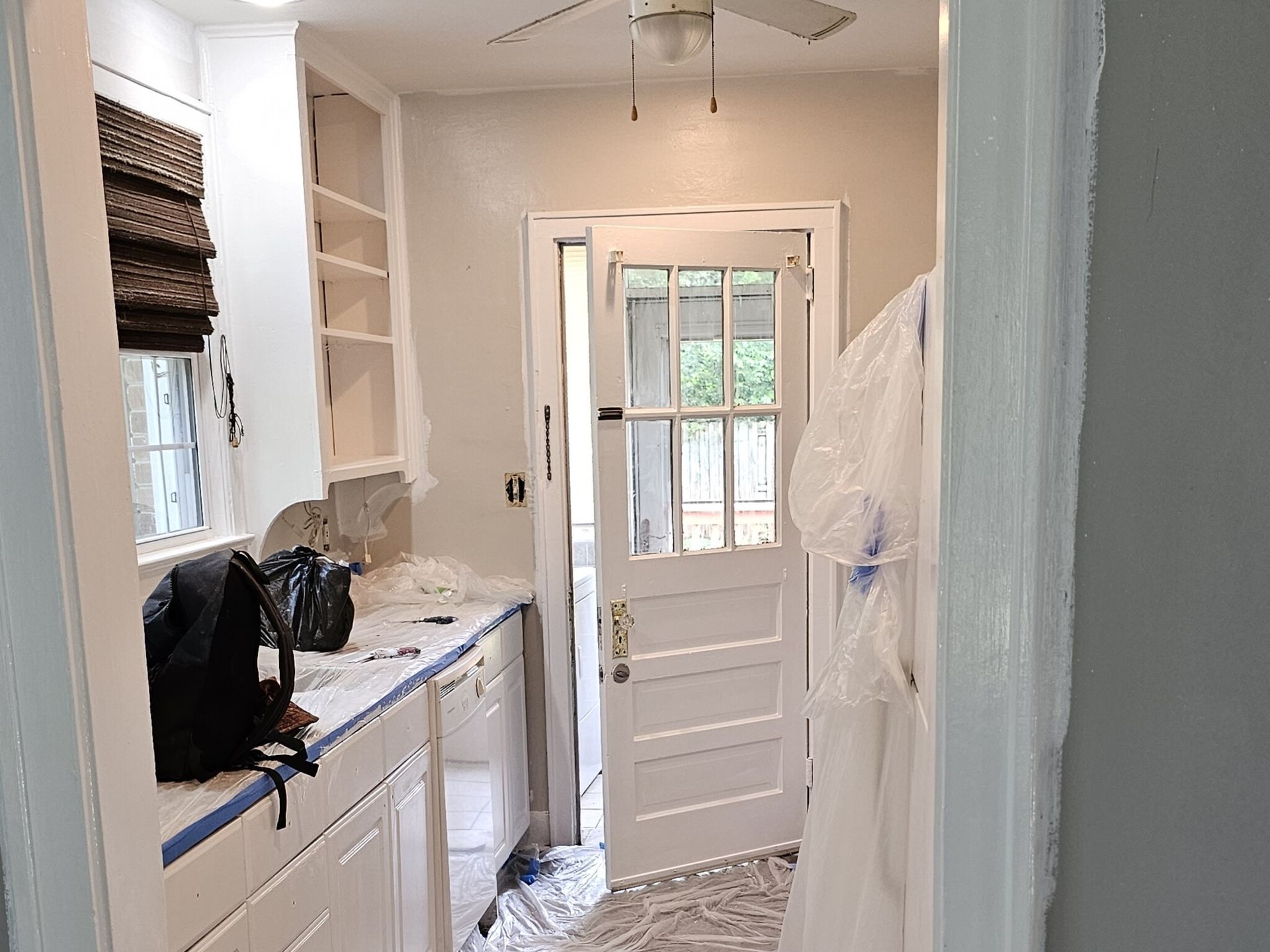 Kitchen with white cabinets, door to backyard, and items covered for painting.