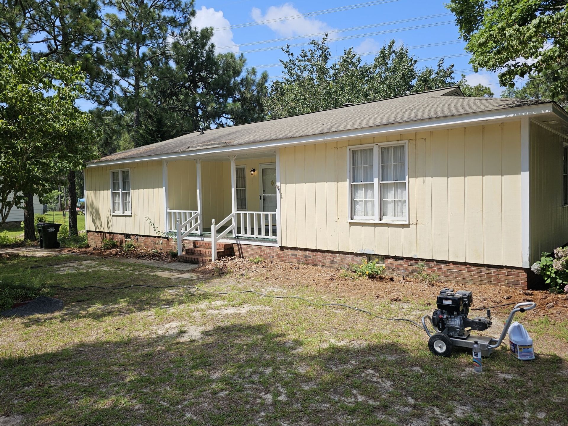 Yellow house with small porch and lawn, paint sprayer in foreground.