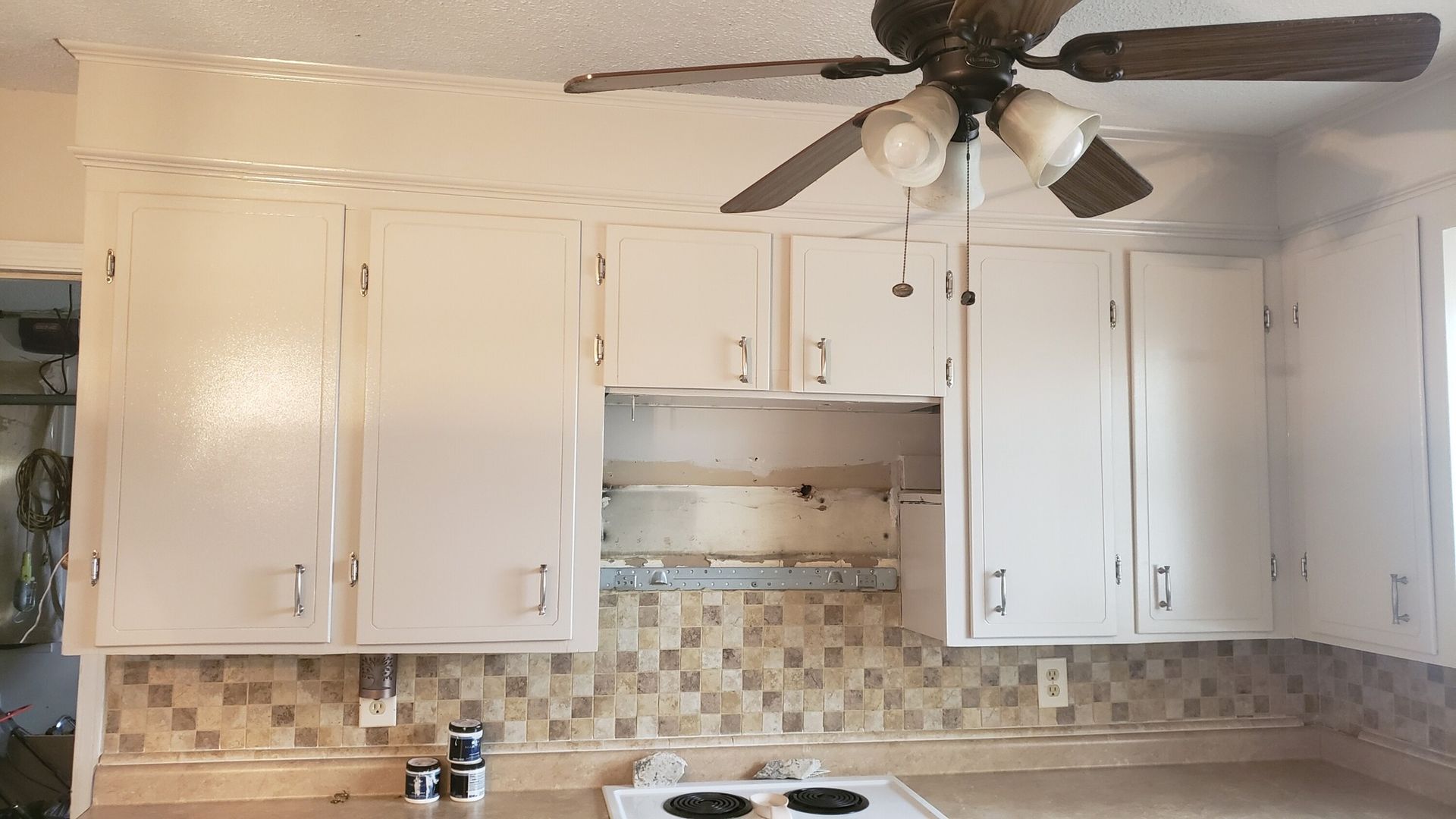 Kitchen with white cabinets, tiled backsplash, and a ceiling fan.