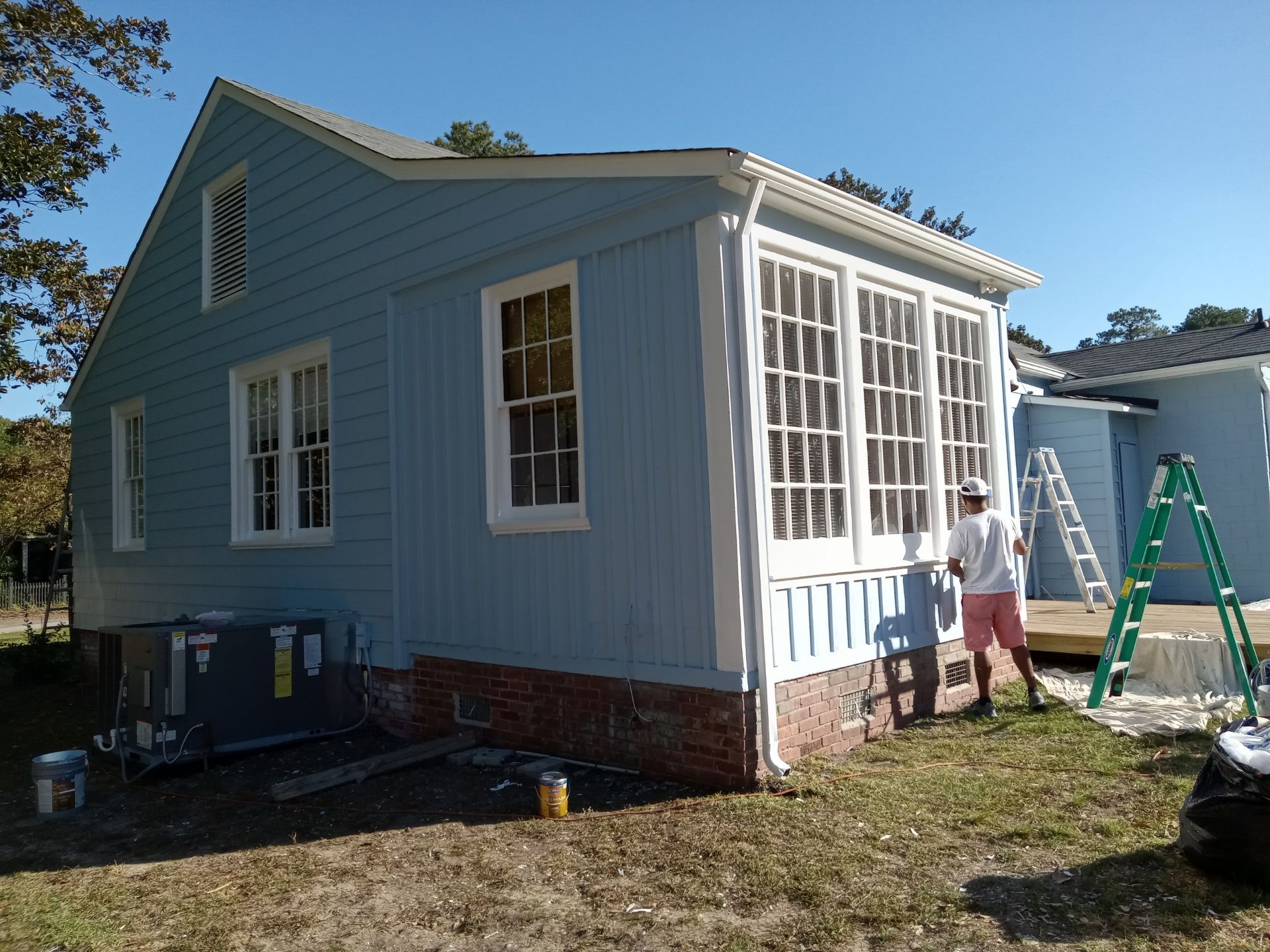 A light blue house with white trim; a person paints the windows.