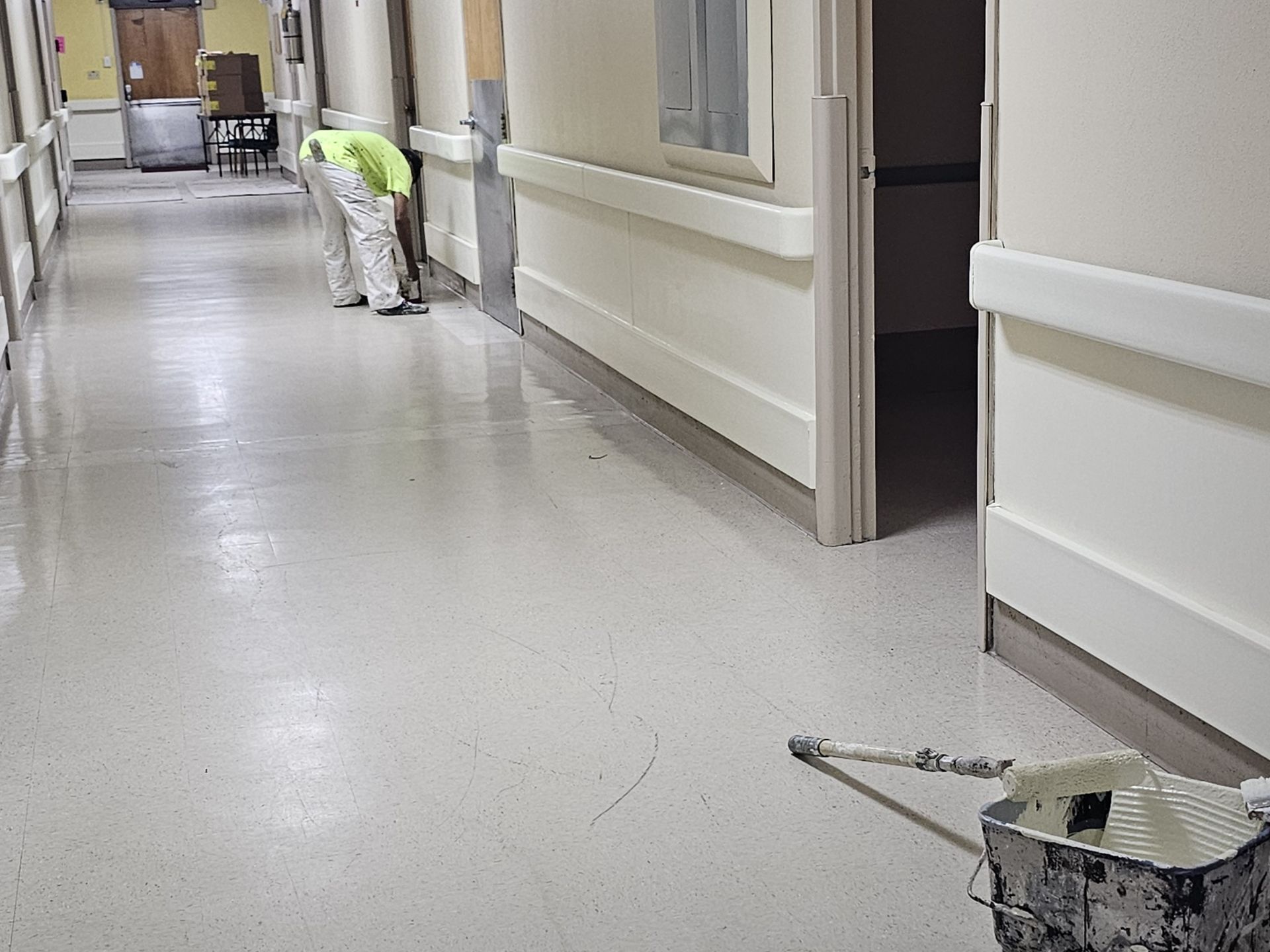 Person painting a hallway floor in a building, with a paint tray on the floor.