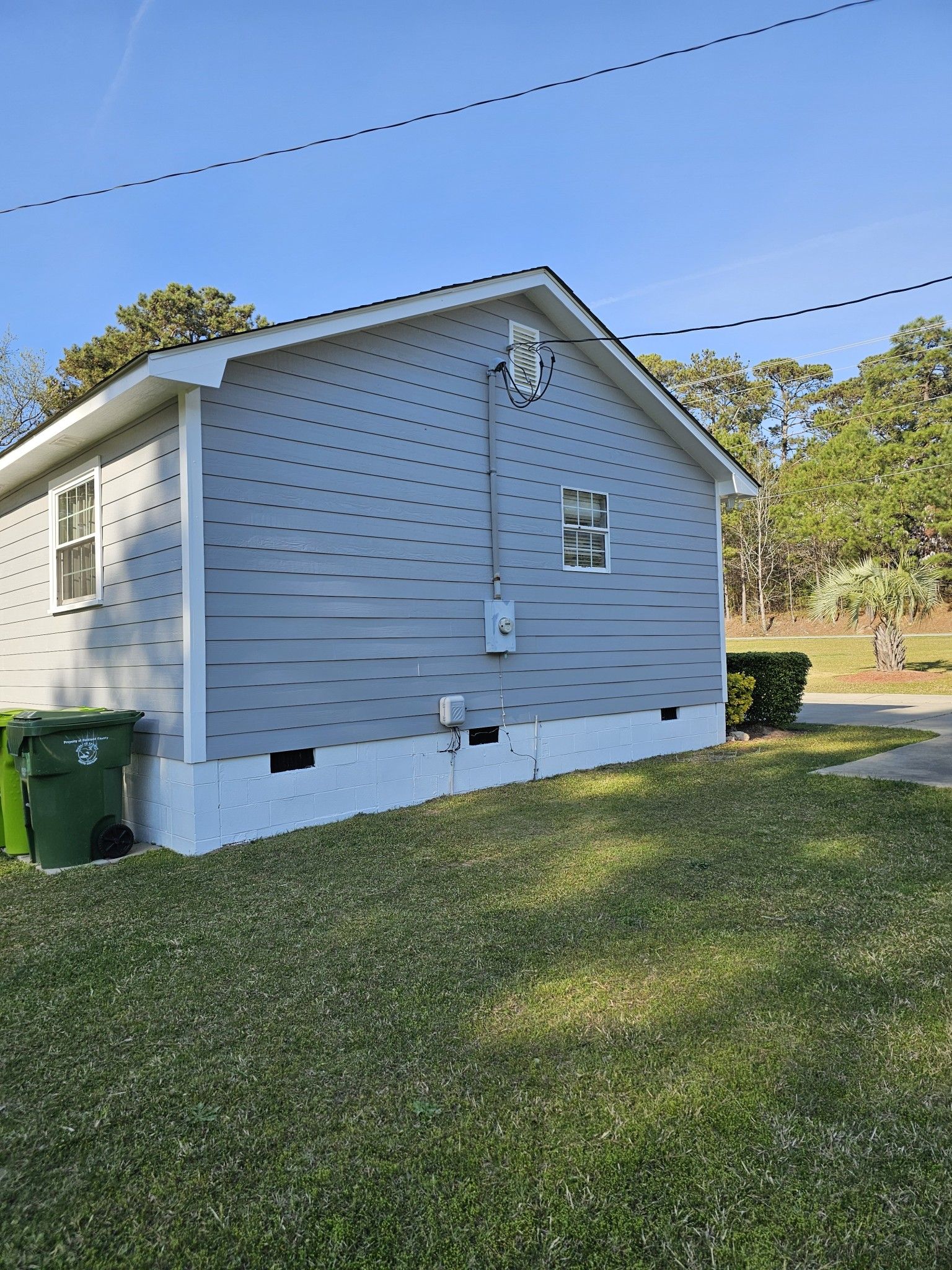 Side view of a gray house with white trim and blue siding, set on grass with a clear sky.