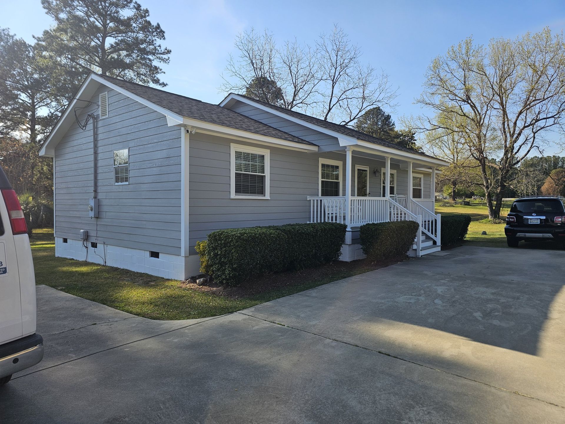 Gray house with white trim, porch, and bushes. A van and car are parked in the driveway.