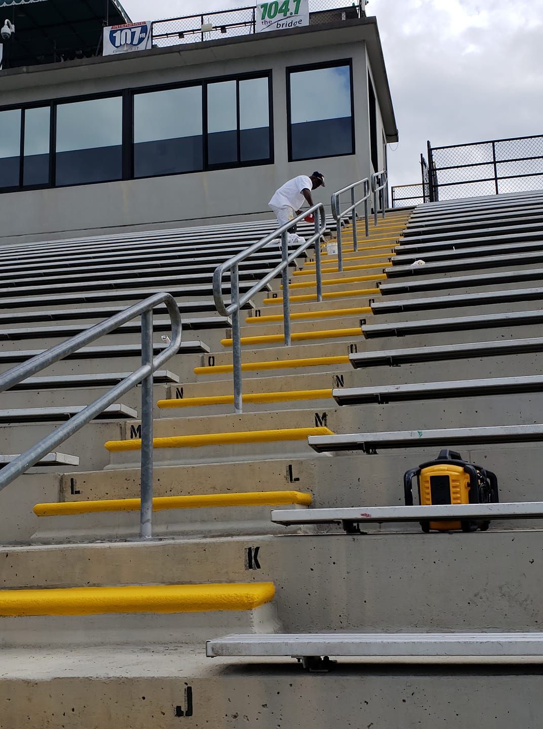 Person climbs stadium stairs, marked with yellow, to a booth. A level sits on the steps.