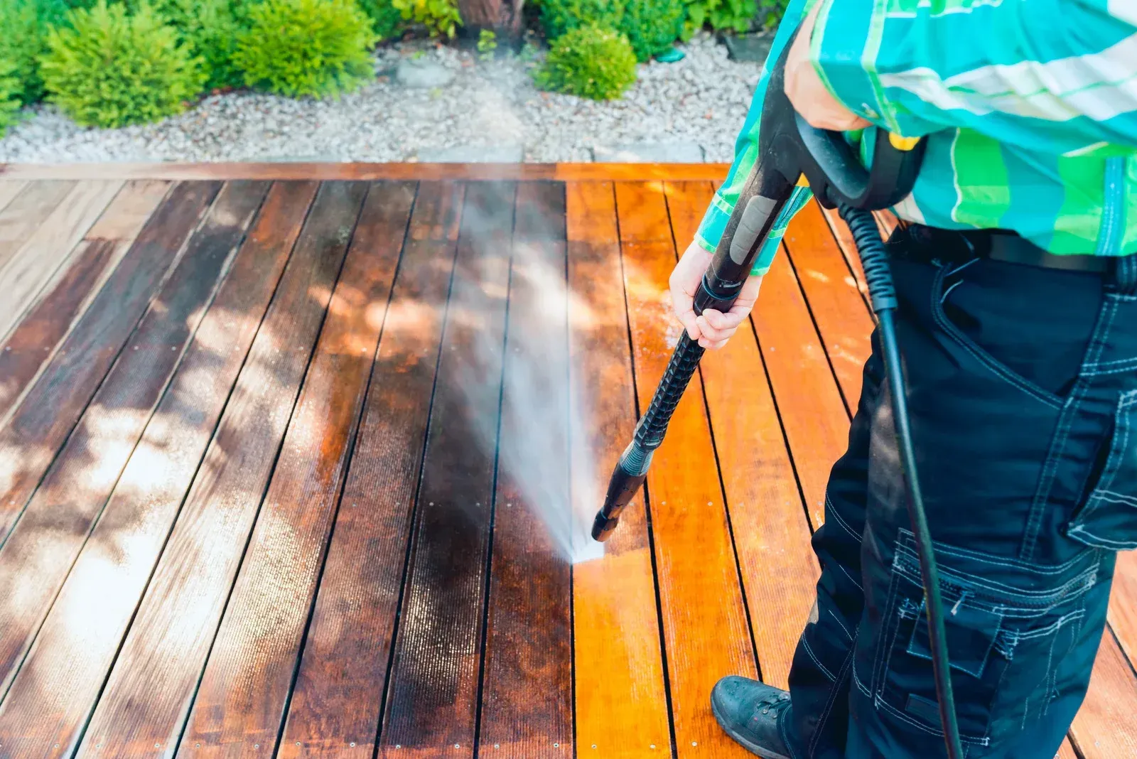 Person power washing a wooden deck, cleaning half of it to reveal the brighter wood.