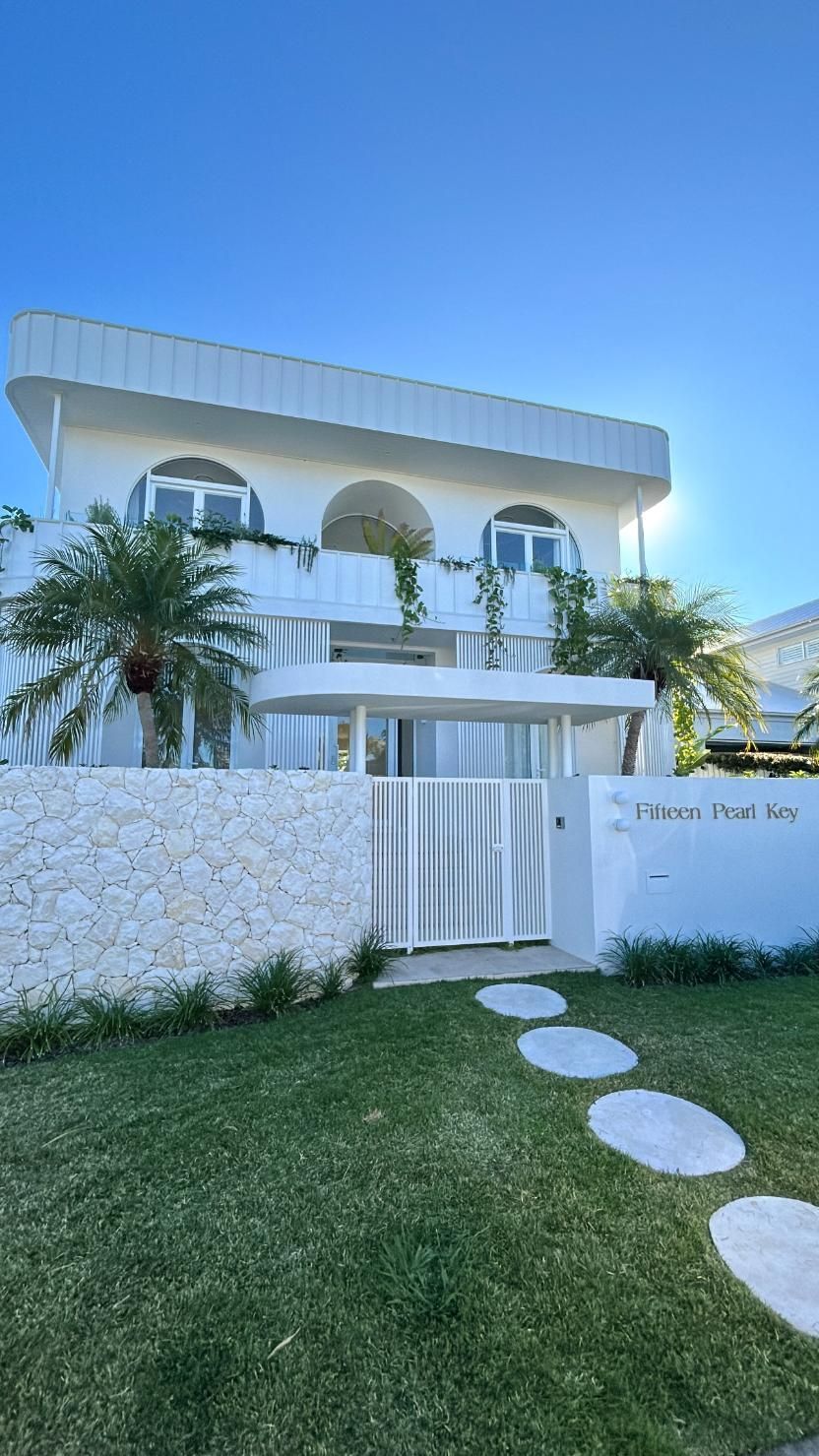 A two-story white building with arched windows, a stone wall, and a stepping stone path leading to a white gate.