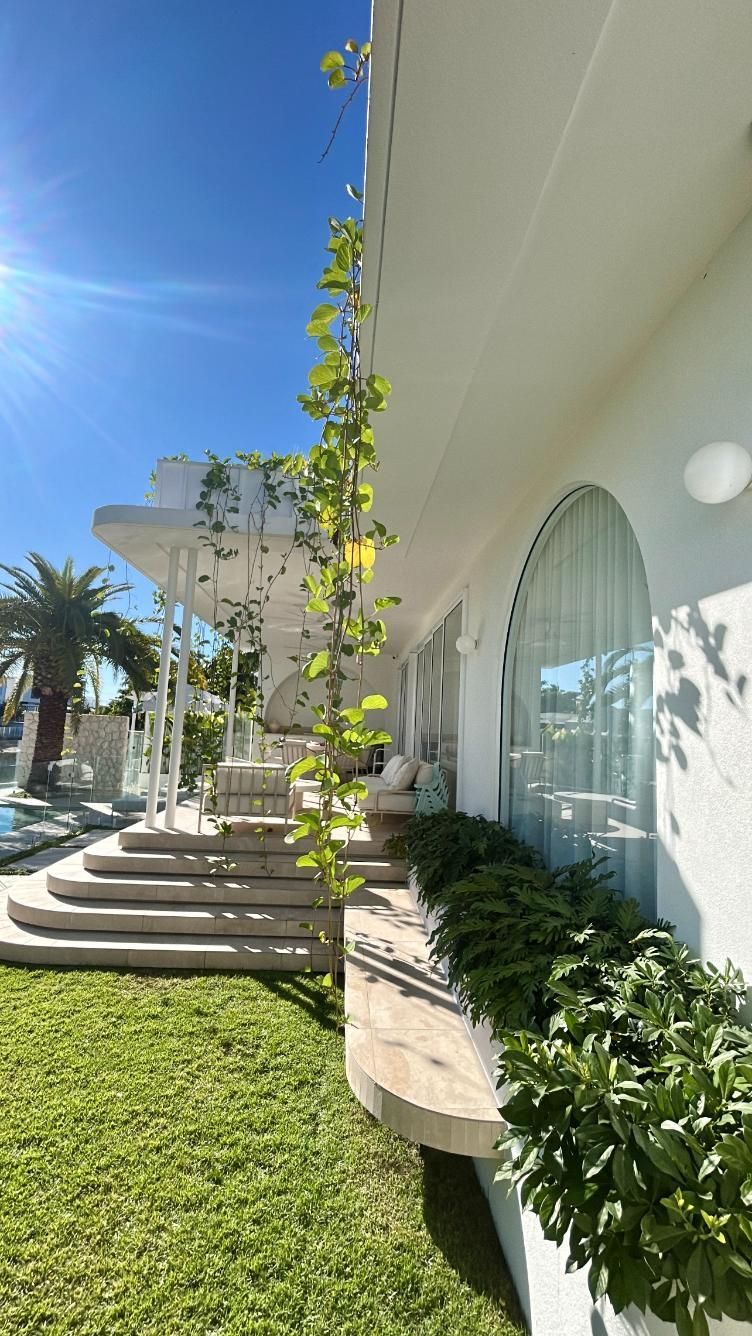 A white house exterior featuring arched windows, stone stairs leading to a patio, and a vibrant climbing vine.