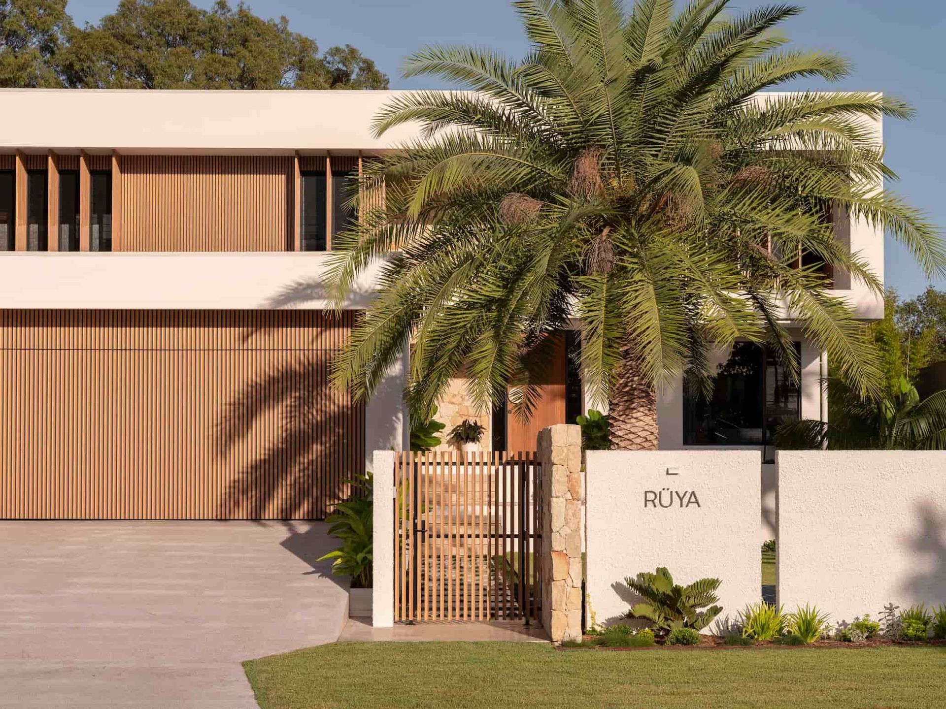 Modern two-story house with wood-slat cladding, a palm tree in the front, and a sign reading 