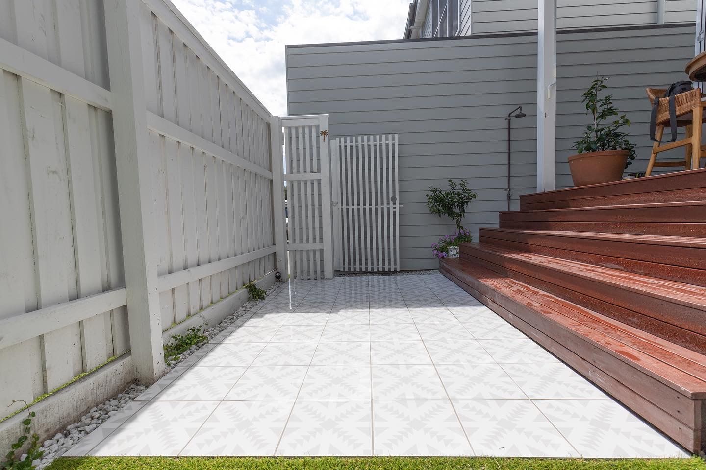 a tiled patio surrounded by a white fence leading up to a deck