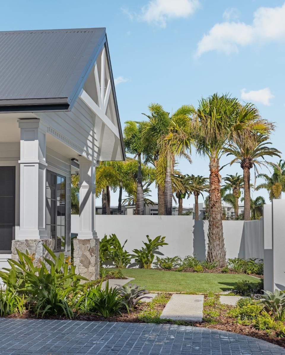 Exterior view of a house with white trim and grey roof, featuring a small landscaped garden with palm trees and pavers.
