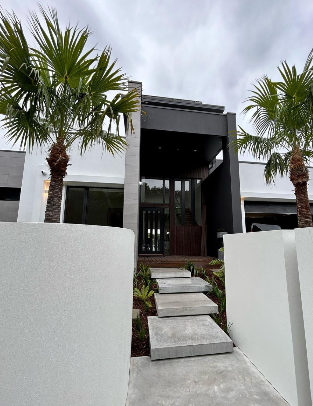 the front of a house with palm trees in front of it and floating concrete steps