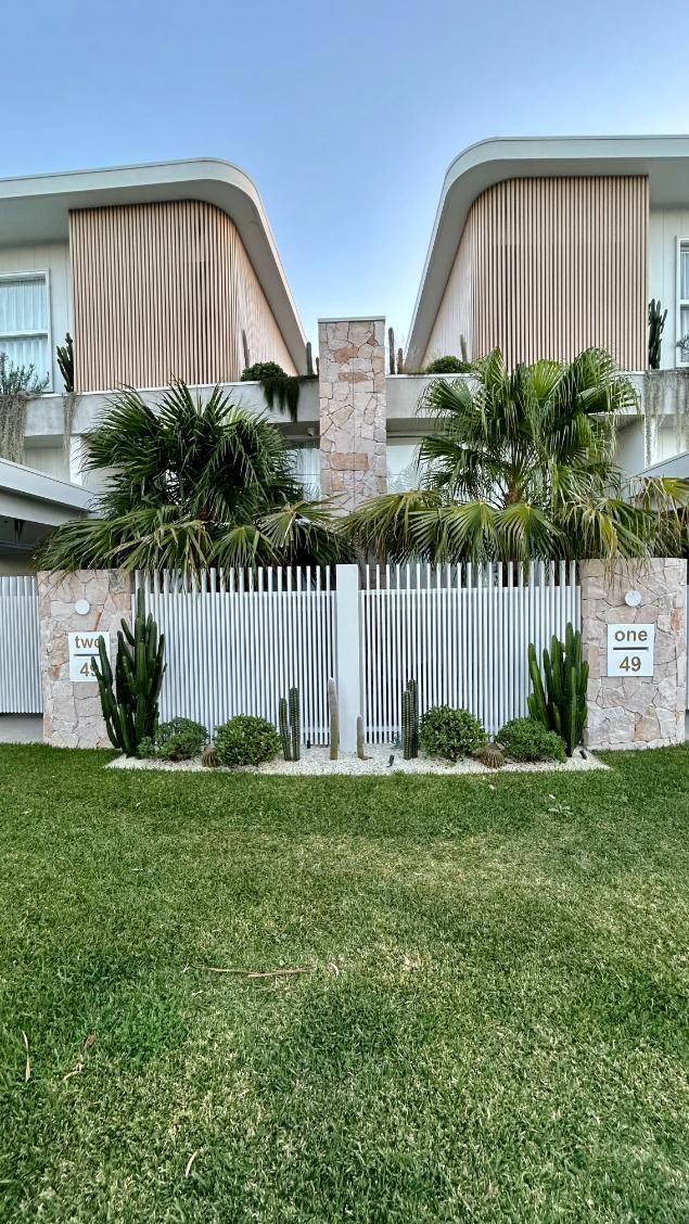 A two-story building with a light-colored facade, decorative wavy accents, a stone pillar, and a modern gated entrance.