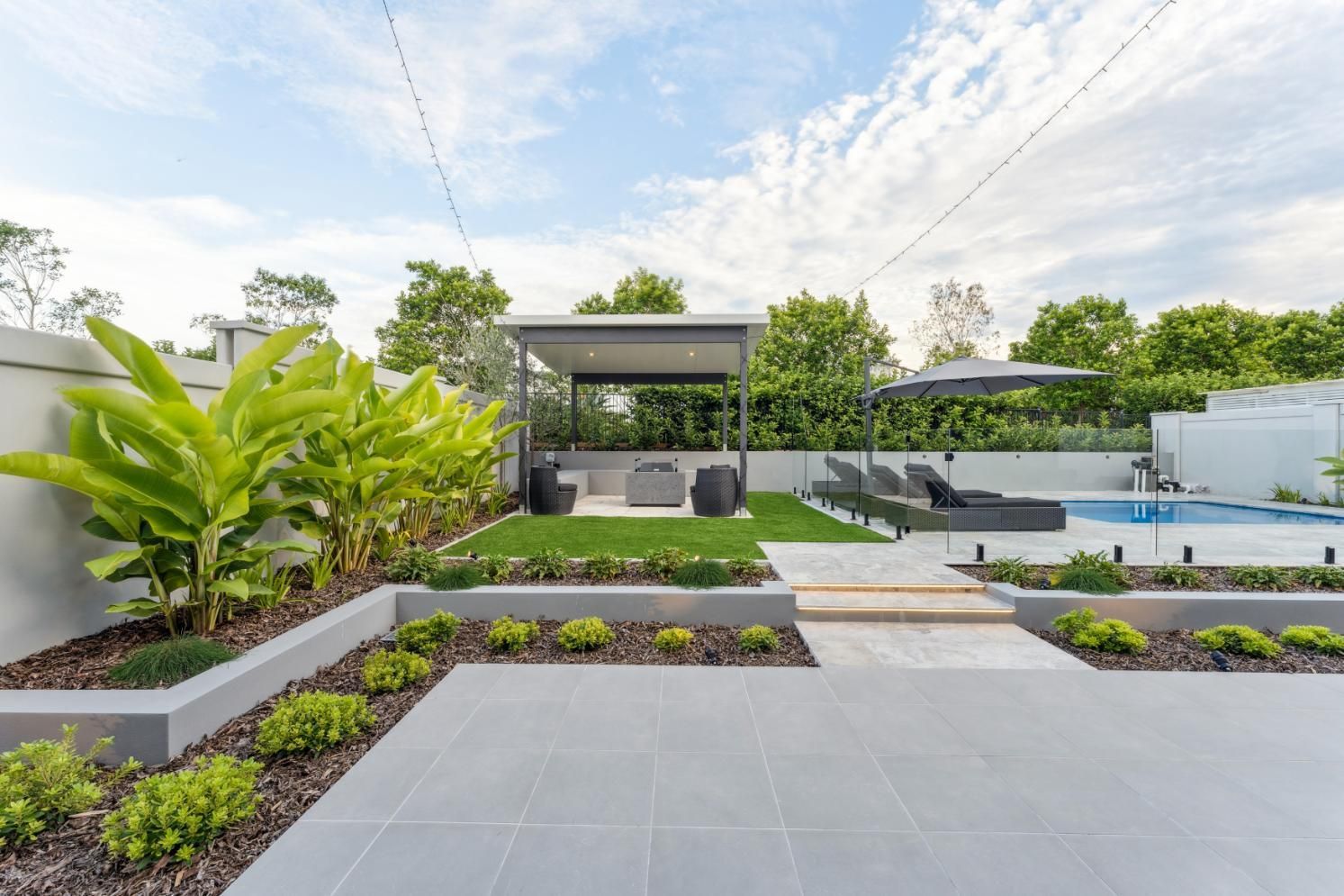 A modern backyard featuring a patio, swimming pool, raised garden beds with lush plants, and a covered lounge area.