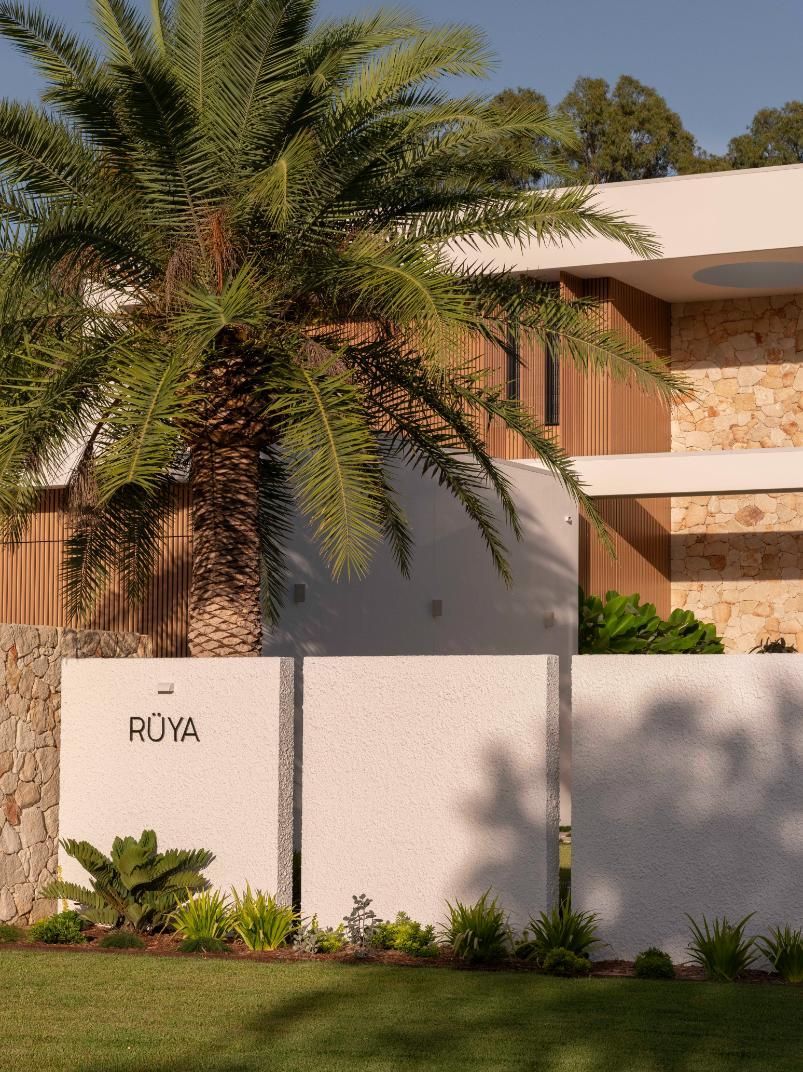 A modern house with stone and wood accents behind a low, white wall featuring the sign 