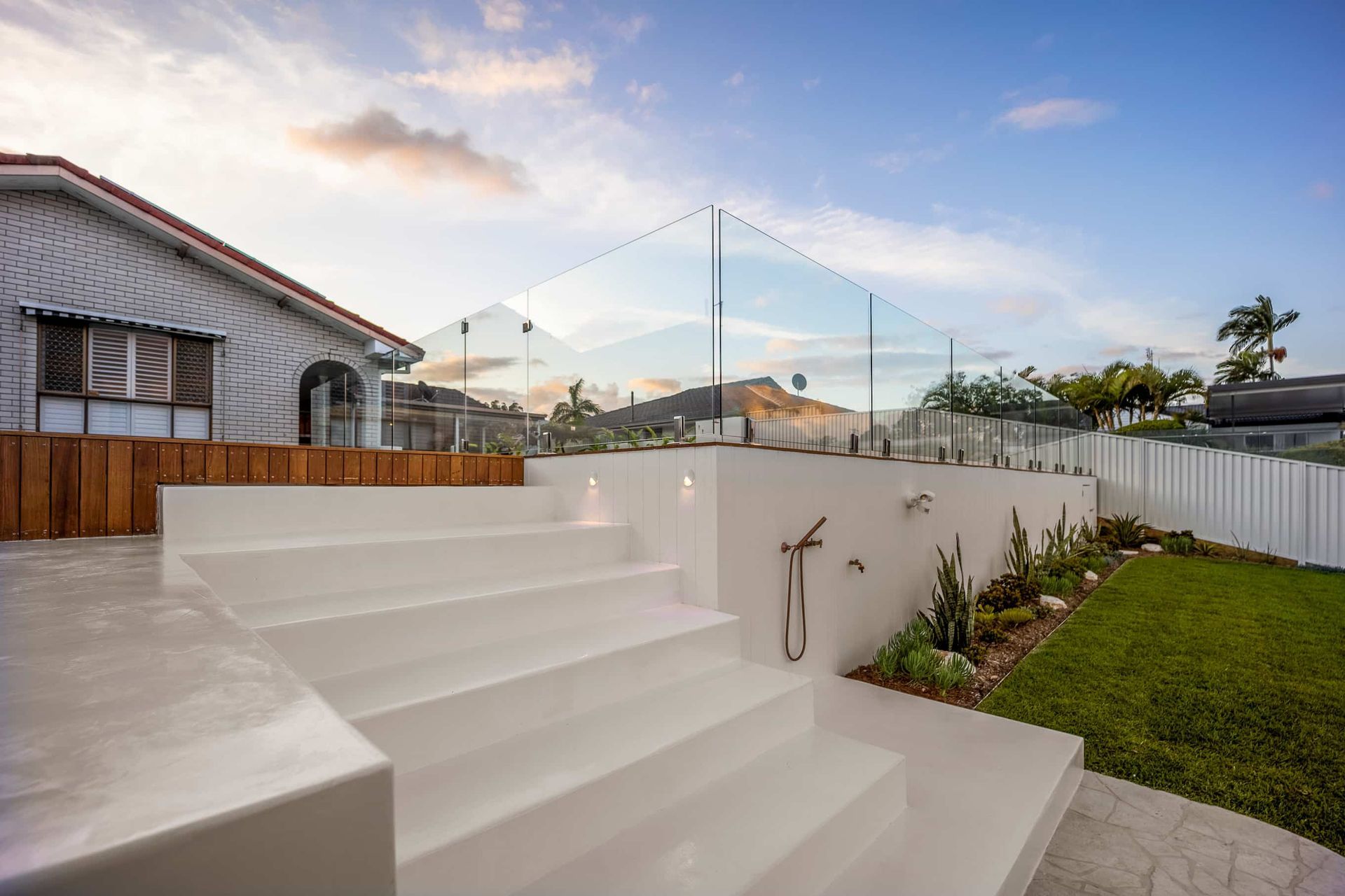 Outdoor white concrete stairs leading to a patio with a glass railing and a distant mountain view at sunset.