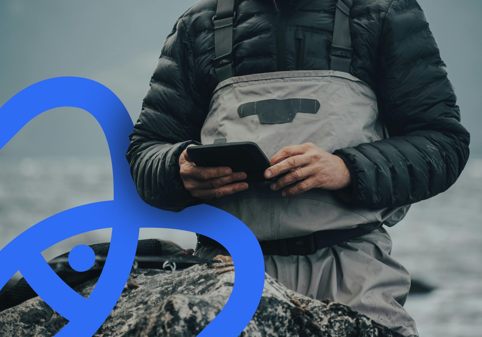 Personne en cuissardes et doudoune, tenant une tablette, debout à l'extérieur.