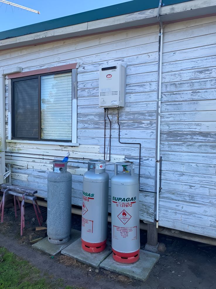 Two Gas Cylinders Are Sitting Outside Of A Building Next To A Window — Casino Plumbing In Casino, NSW