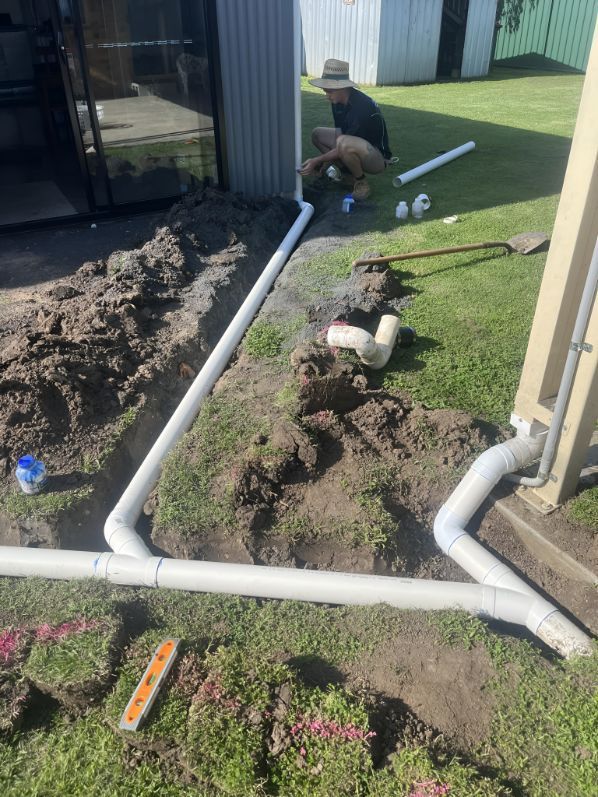 A Man Is Working On A Drainage System In A Backyard — Casino Plumbing In Casino, NSW