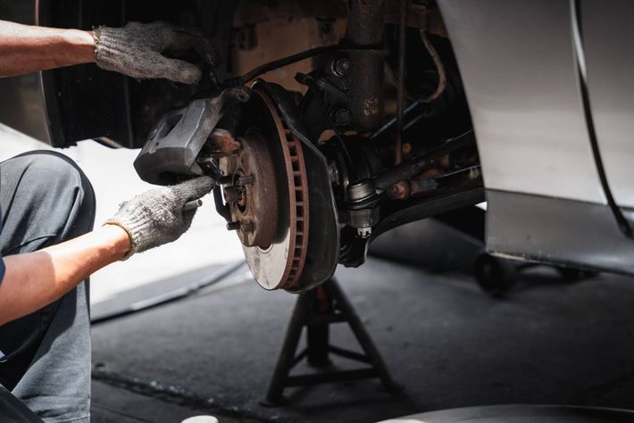 Person in gloves working on a car's brake system, wheel removed, supported by a jack stand.