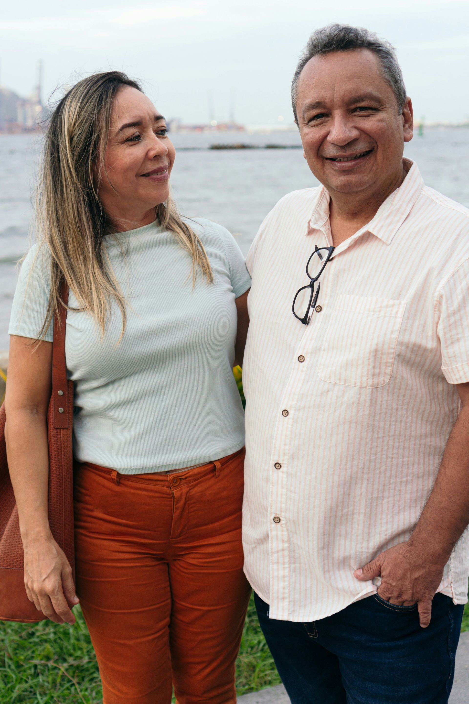 A woman wearing a floral shirt and jeans is smiling.