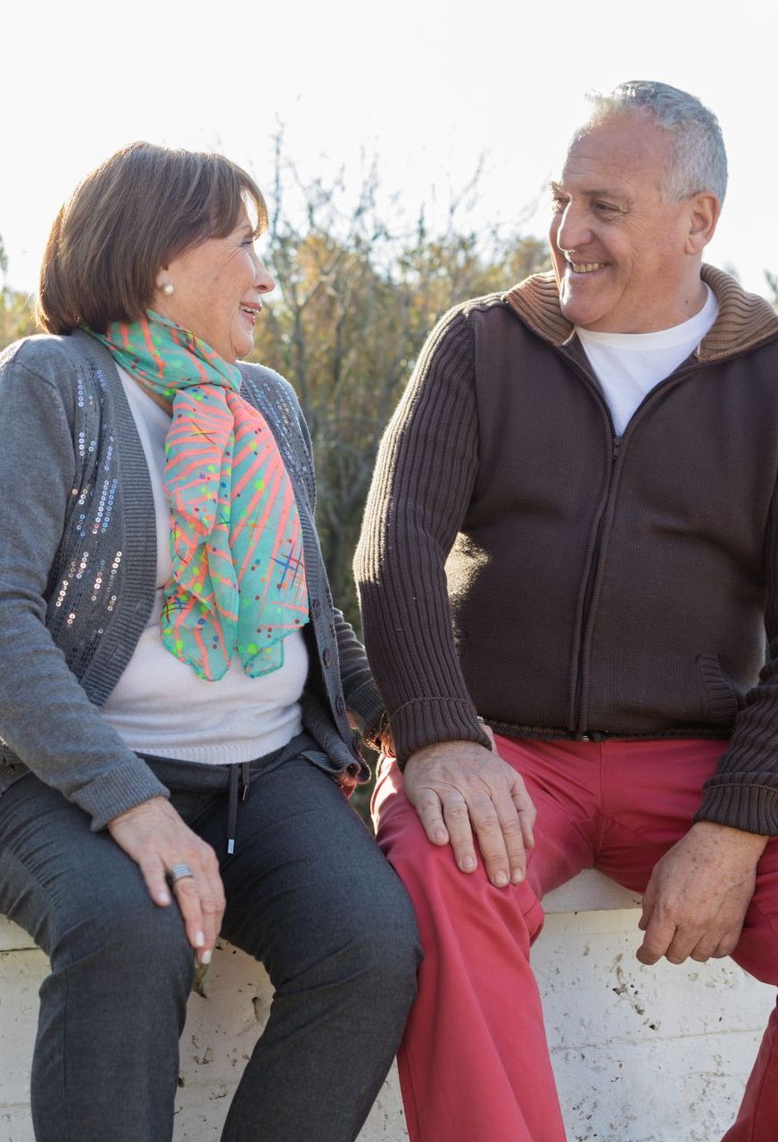 A woman wearing a floral shirt and jeans is smiling.