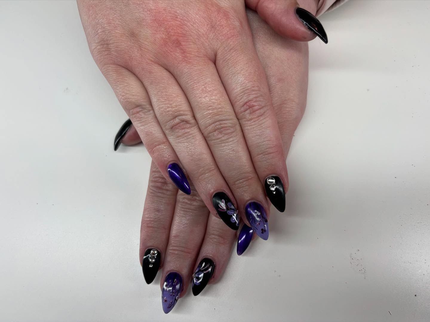 A close up of a woman 's hands with purple and black nails.