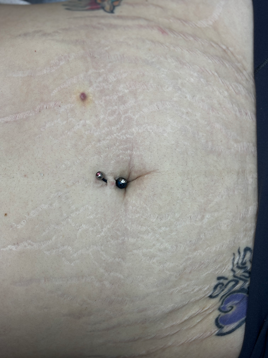A close up of a woman 's belly with a navel piercing and a tattoo.